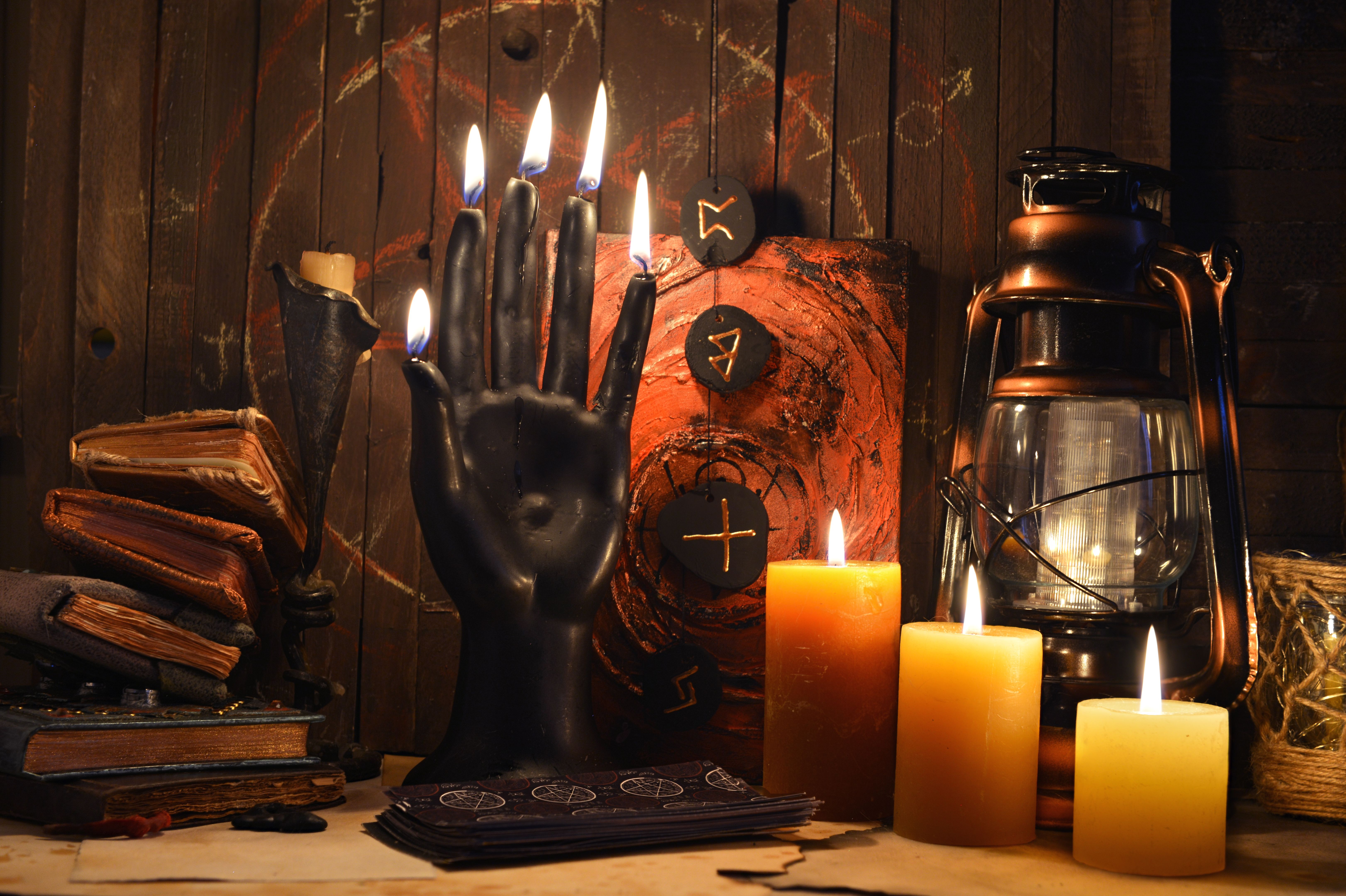 Mystic still life with black candle as scary hand, magic spell book, old lamp and witchy ritual objects on altar table. Occult, esoteric, wicca, Halloween and gothic concept.
