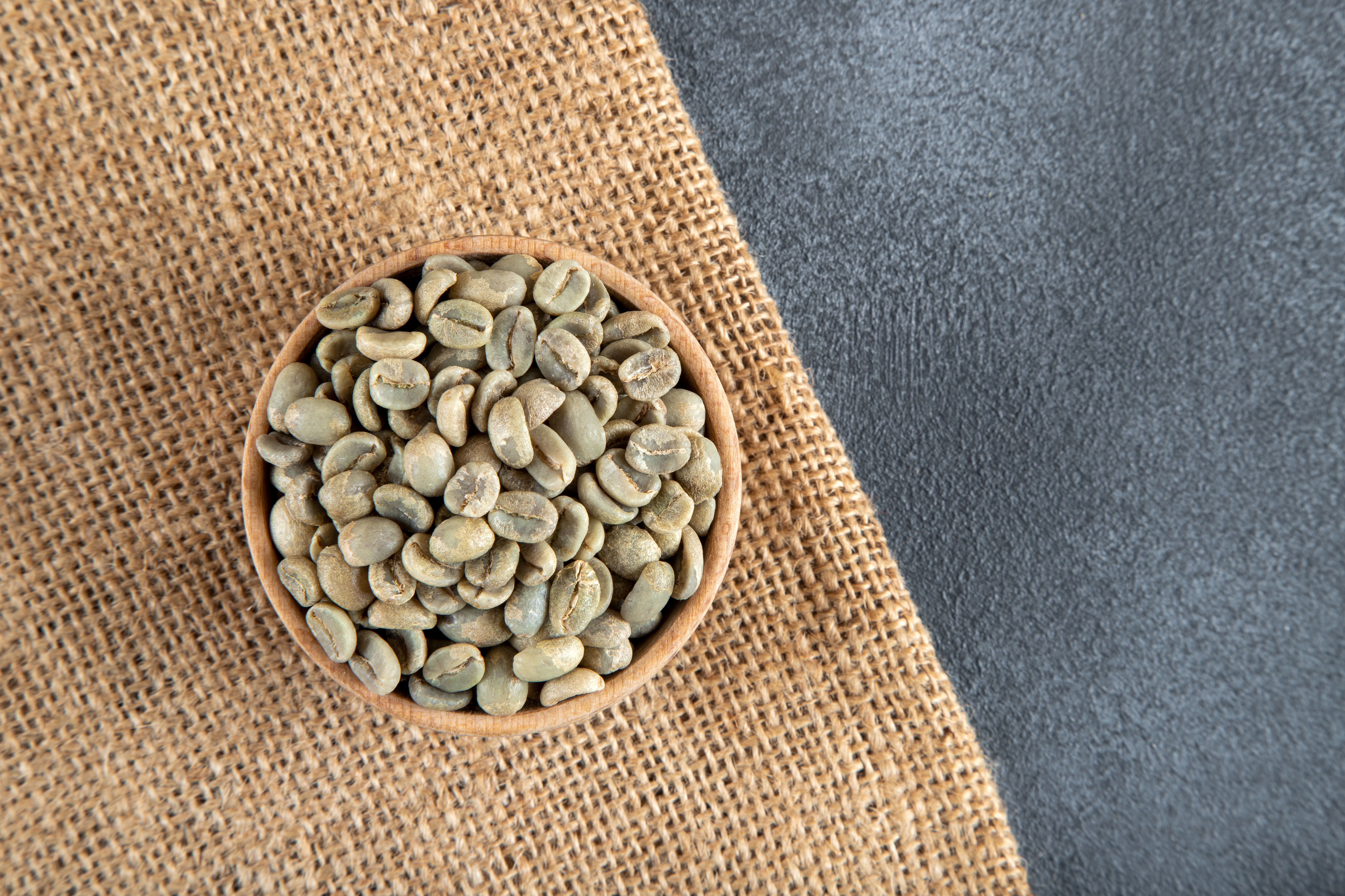 A bowl full of green coffee beans on burlap sack