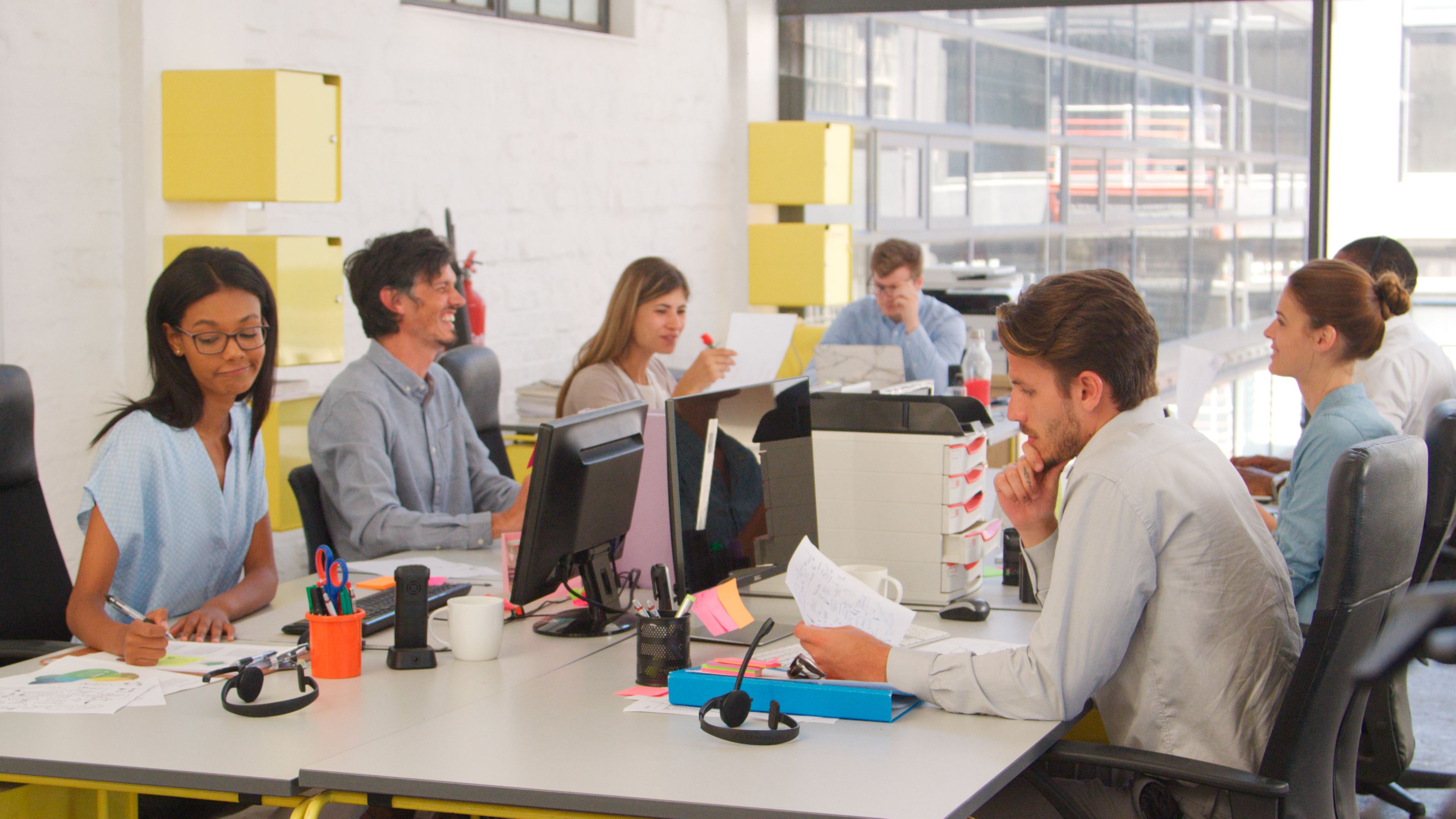 Business Team Sitting At Desks In Open Plan Office Working At Computers And Discussing Documents