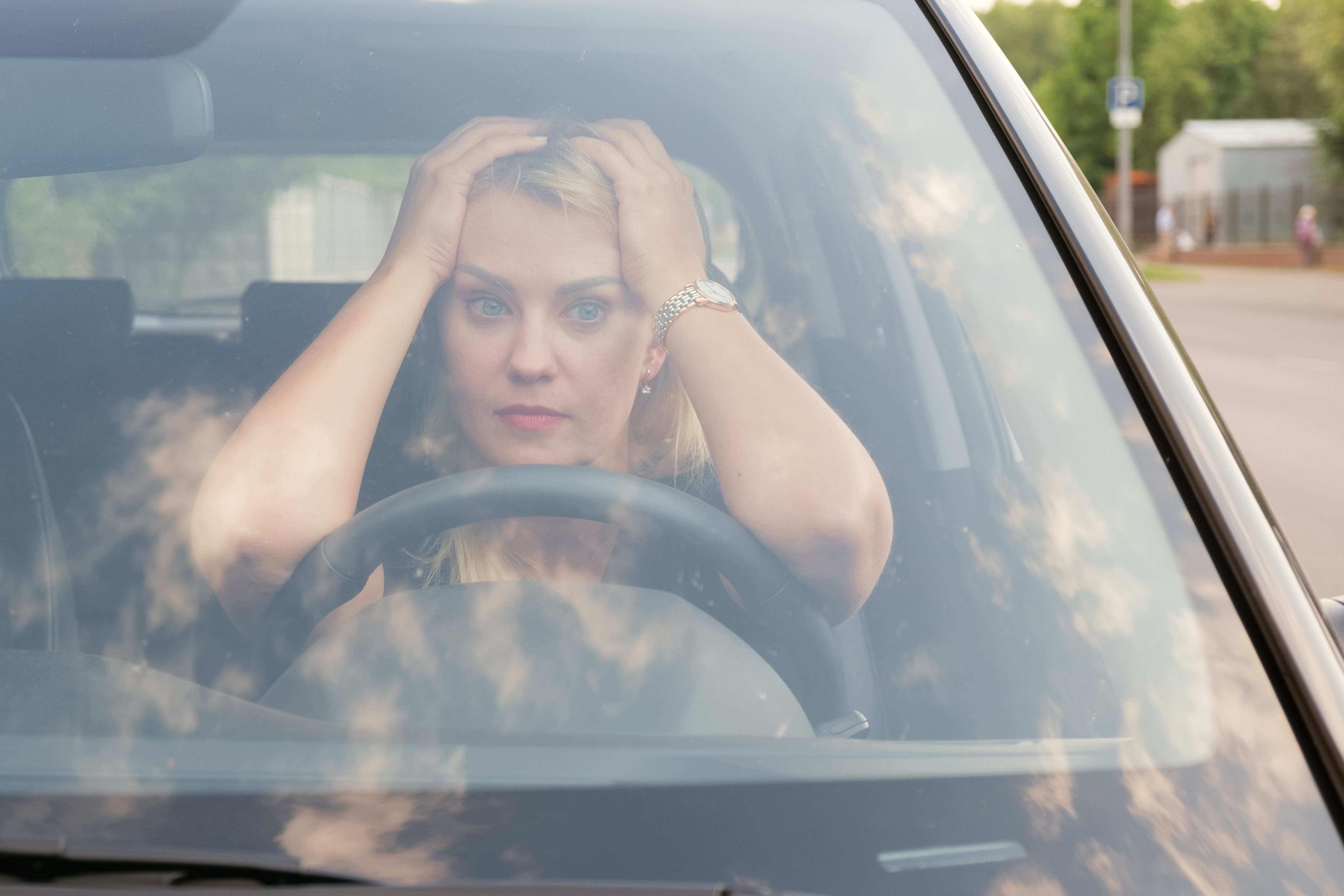 Attractive woman with blond hair put her hands and head on the steering wheel and looks forward sadly