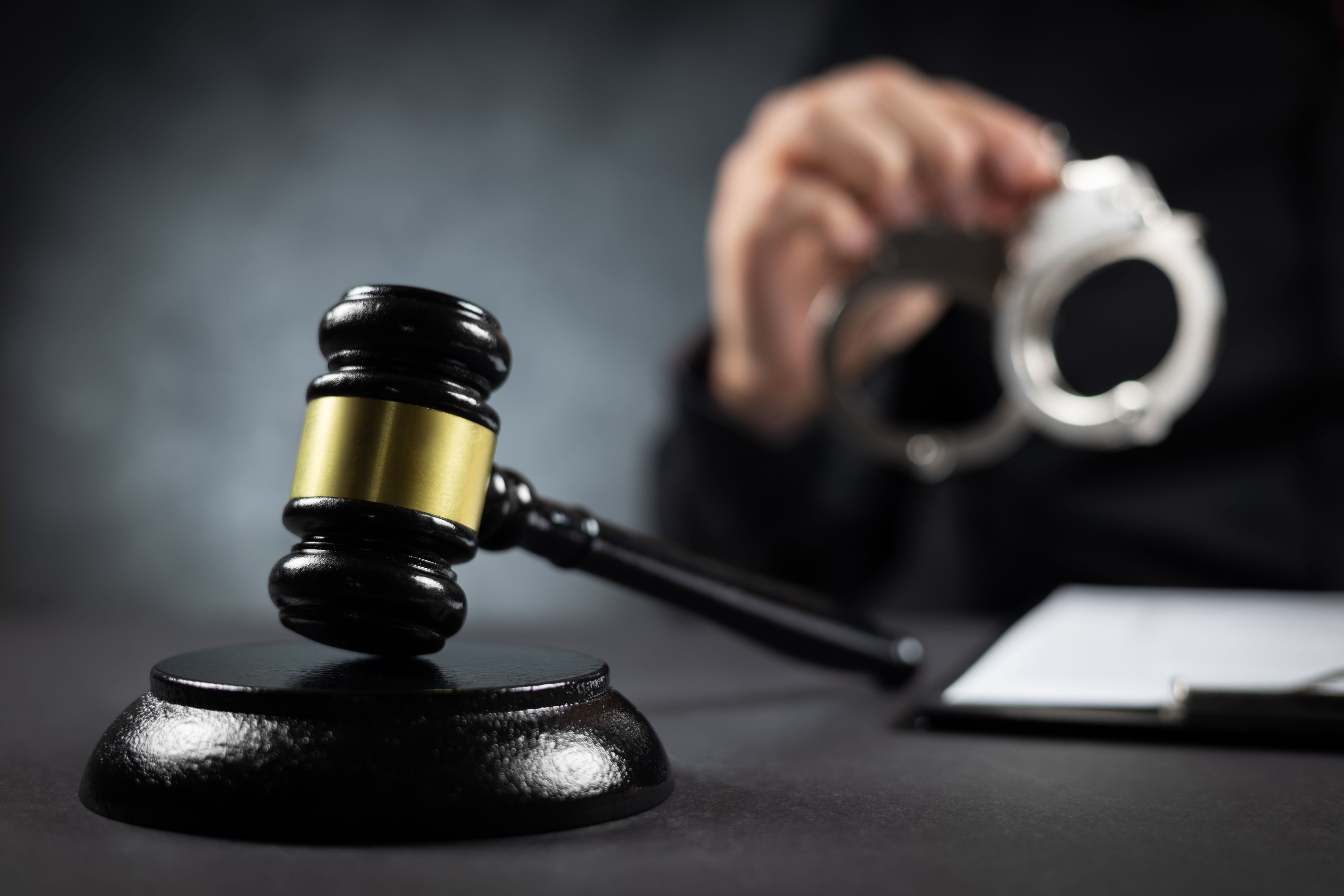 Judge's gavel and handcuffs in hand on a dark background. Judge's gavel and handcuffs