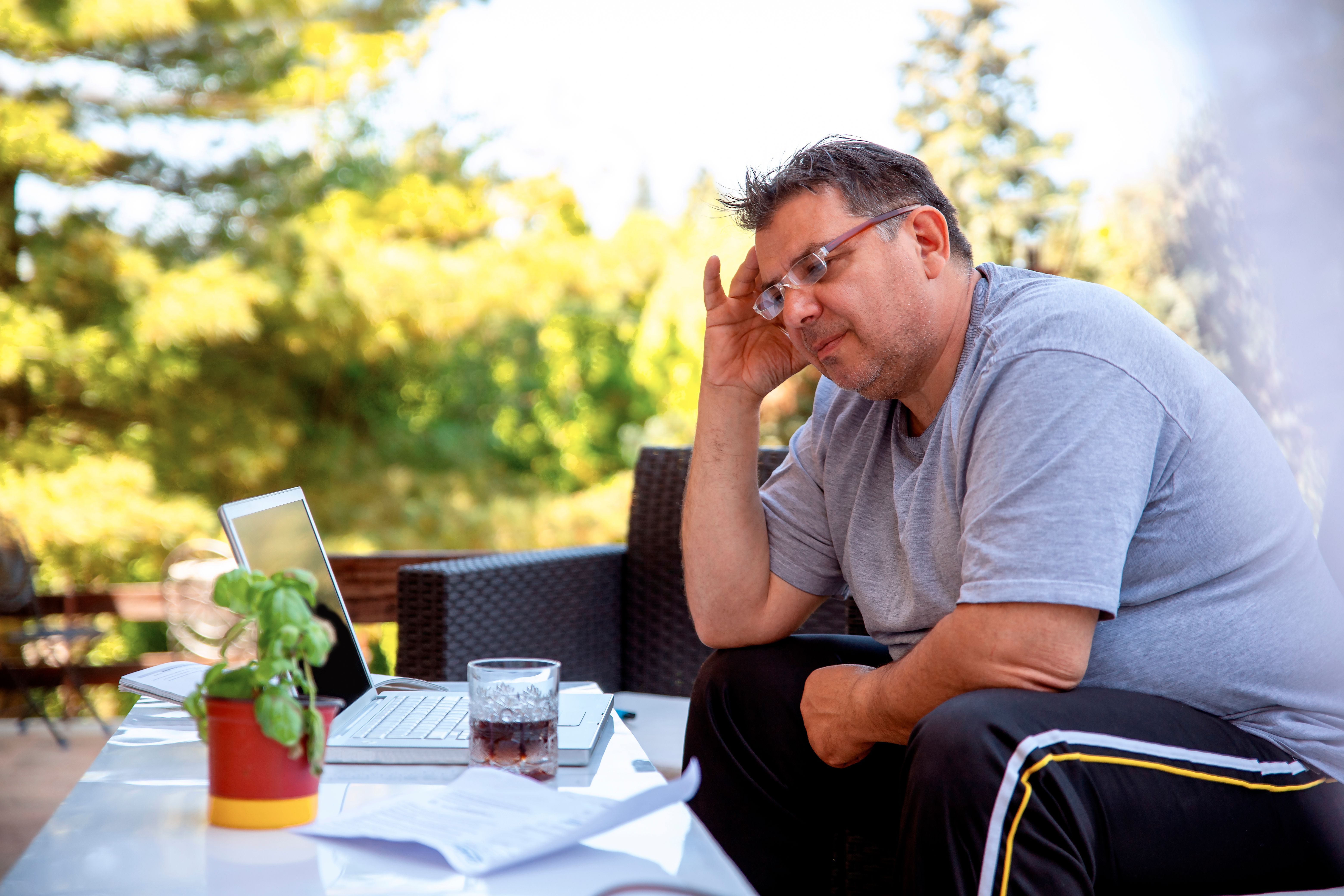Close up of a mid adult man using a laptop drinking glass of whiskey
