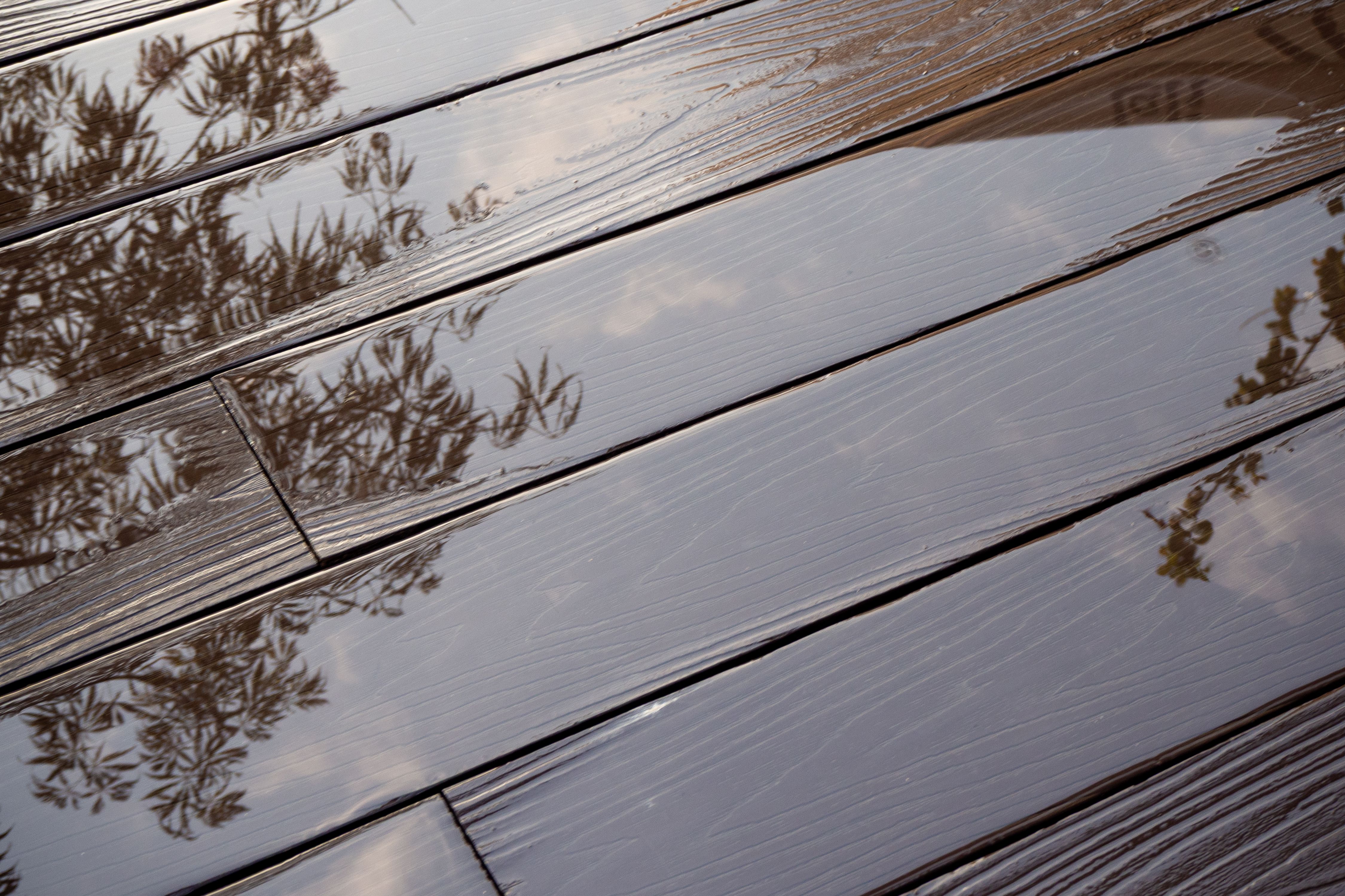 Tree reflection puddles on plastic composite decking with wood grain. Long-lasting, beautiful, durable and waterproof outdoor floor covering