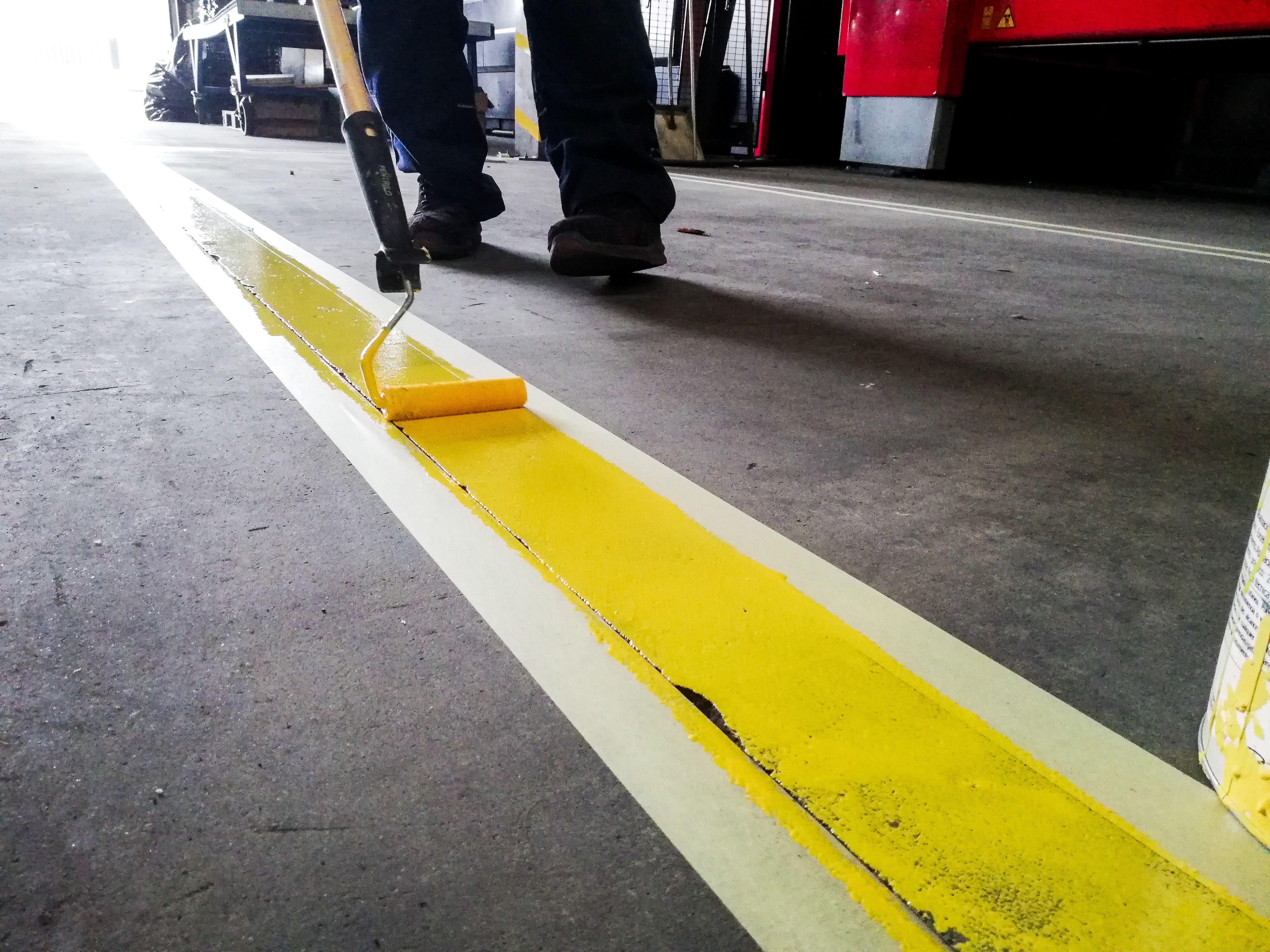 Closeup of a person painting a yellow line on a garage floor under the lights Closeup of a person painting a yellow line on a garage floor under the lights