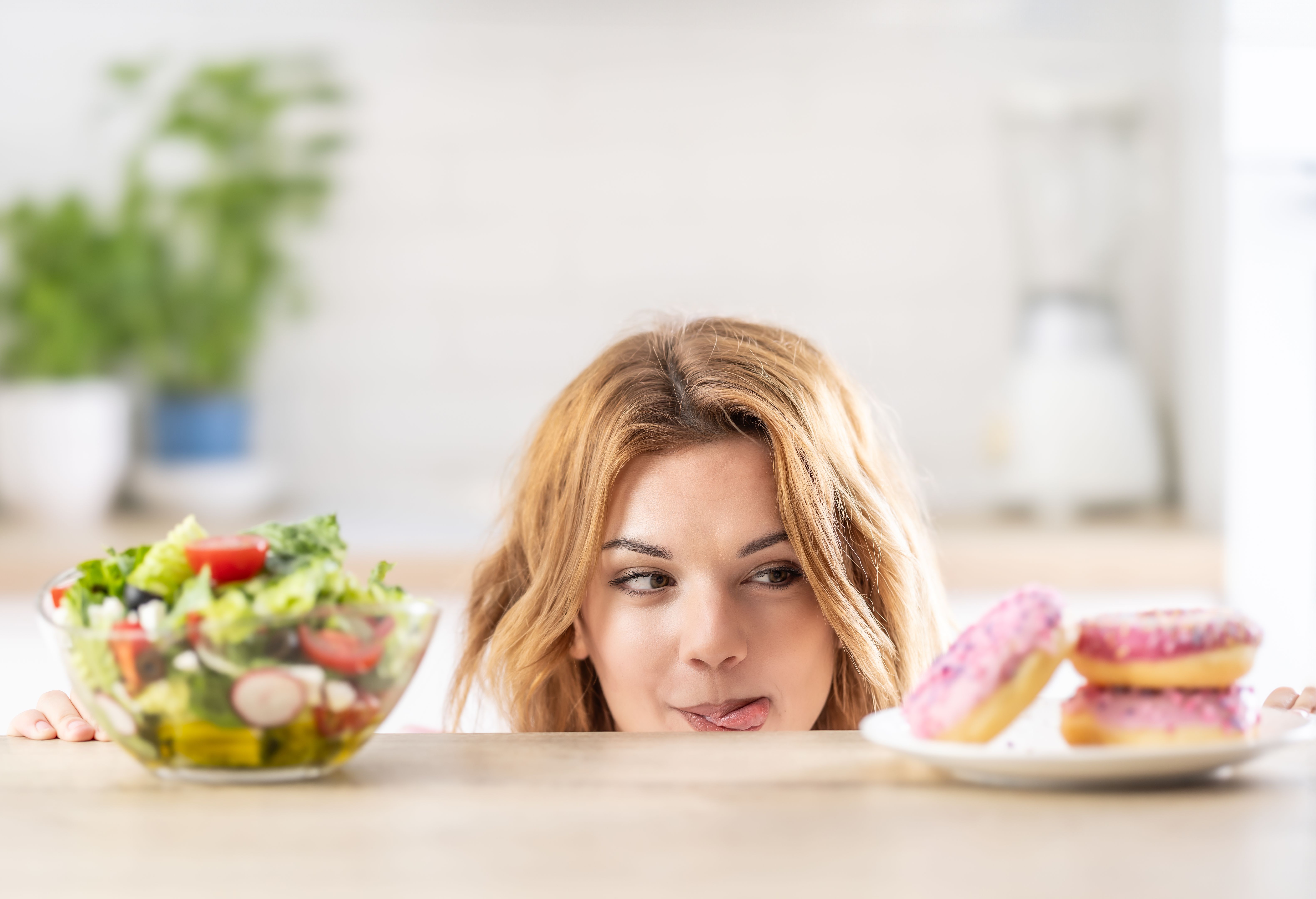 Beautiful young woman tempted having to make choice between fresh lettuce salad and doughnut in healthy unhealthy food, detox eating, calories and diet concept. Beautiful young woman tempted having to make choice between fresh lettuce salad and doughnut in healthy unhealthy food, detox eating, calories and diet concept.