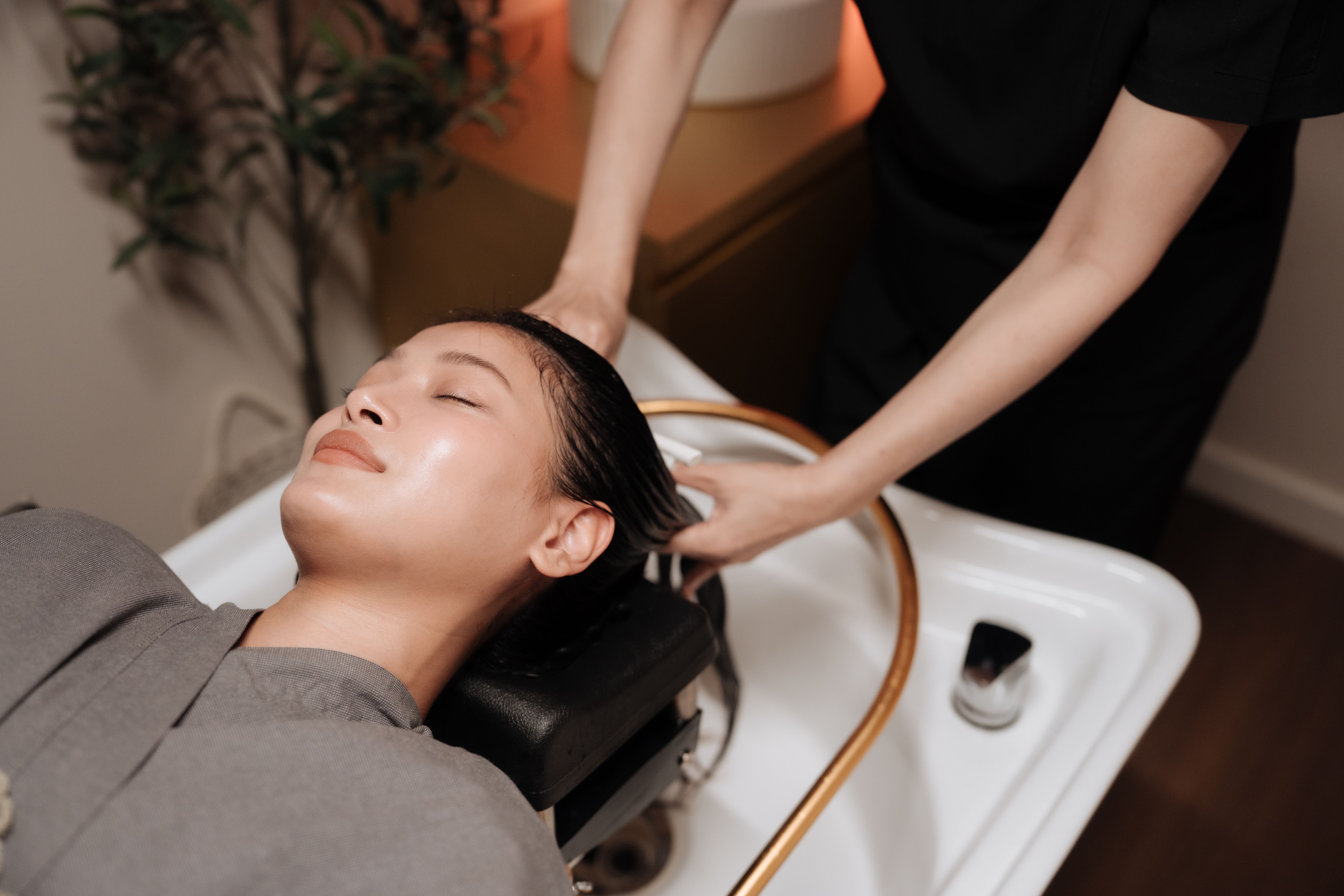 Woman relaxing during a luxurious hair wash and head spa session at a wellness center as gentle streams of warm water flow from the shower ring