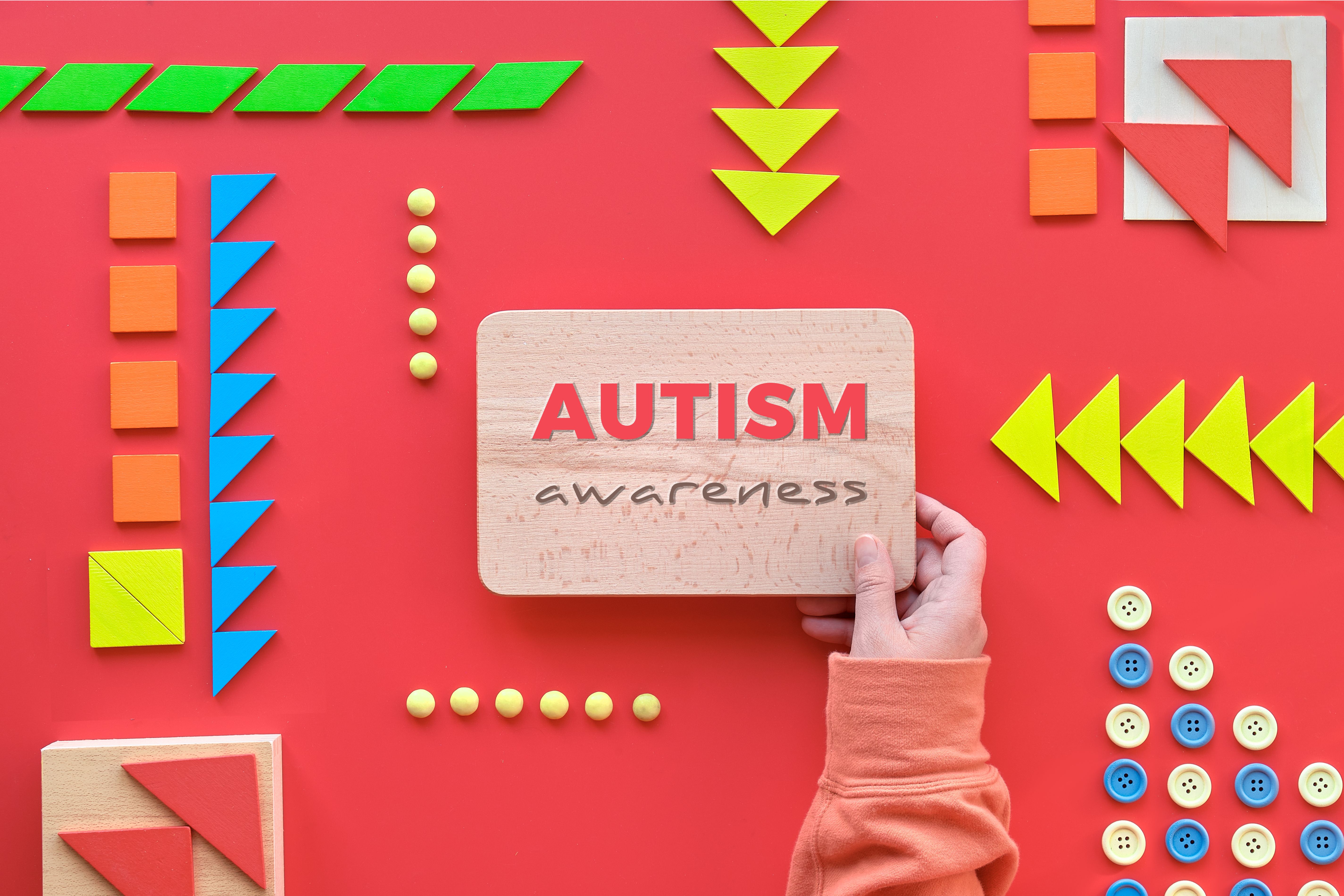 Creative design for Autism World Day, text on wood in hand. Tangram puzzle, flat lay on red