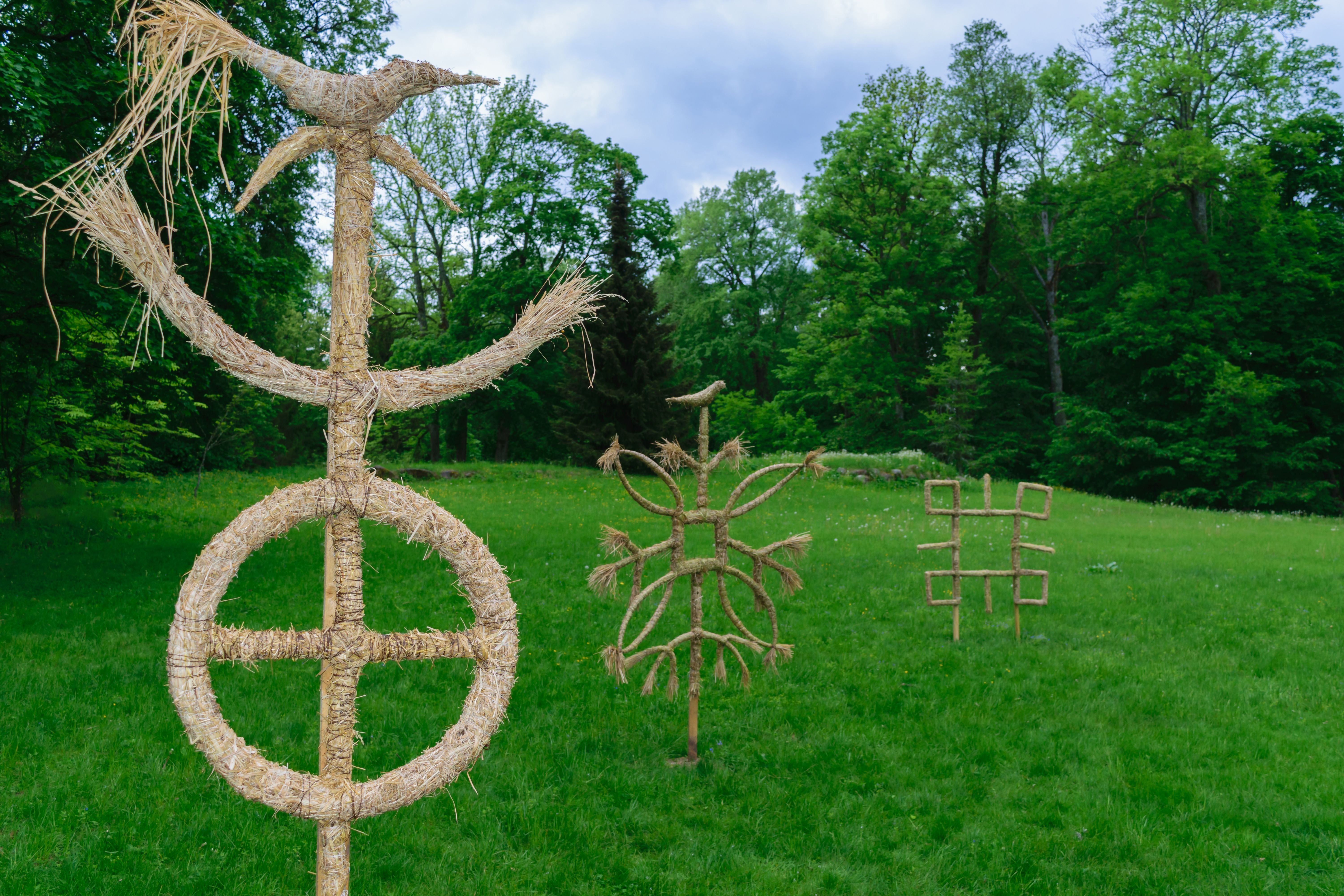 Baltic mythology gods symbols made from straws standing in the green meadow during cloudy day