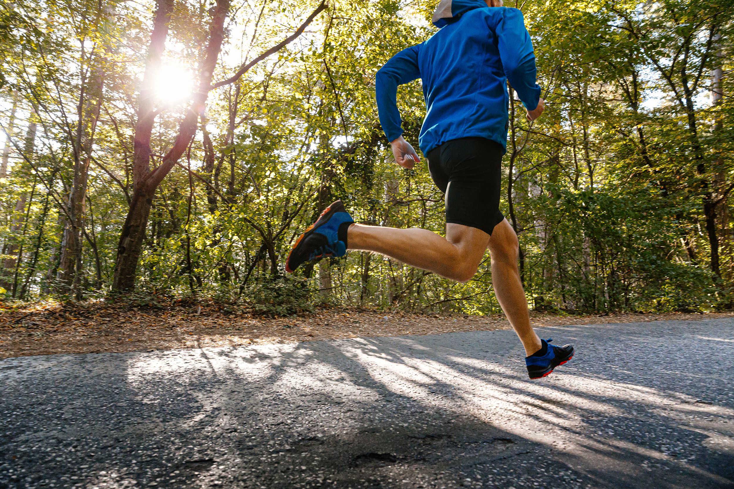 male runner running road in park in light of sun