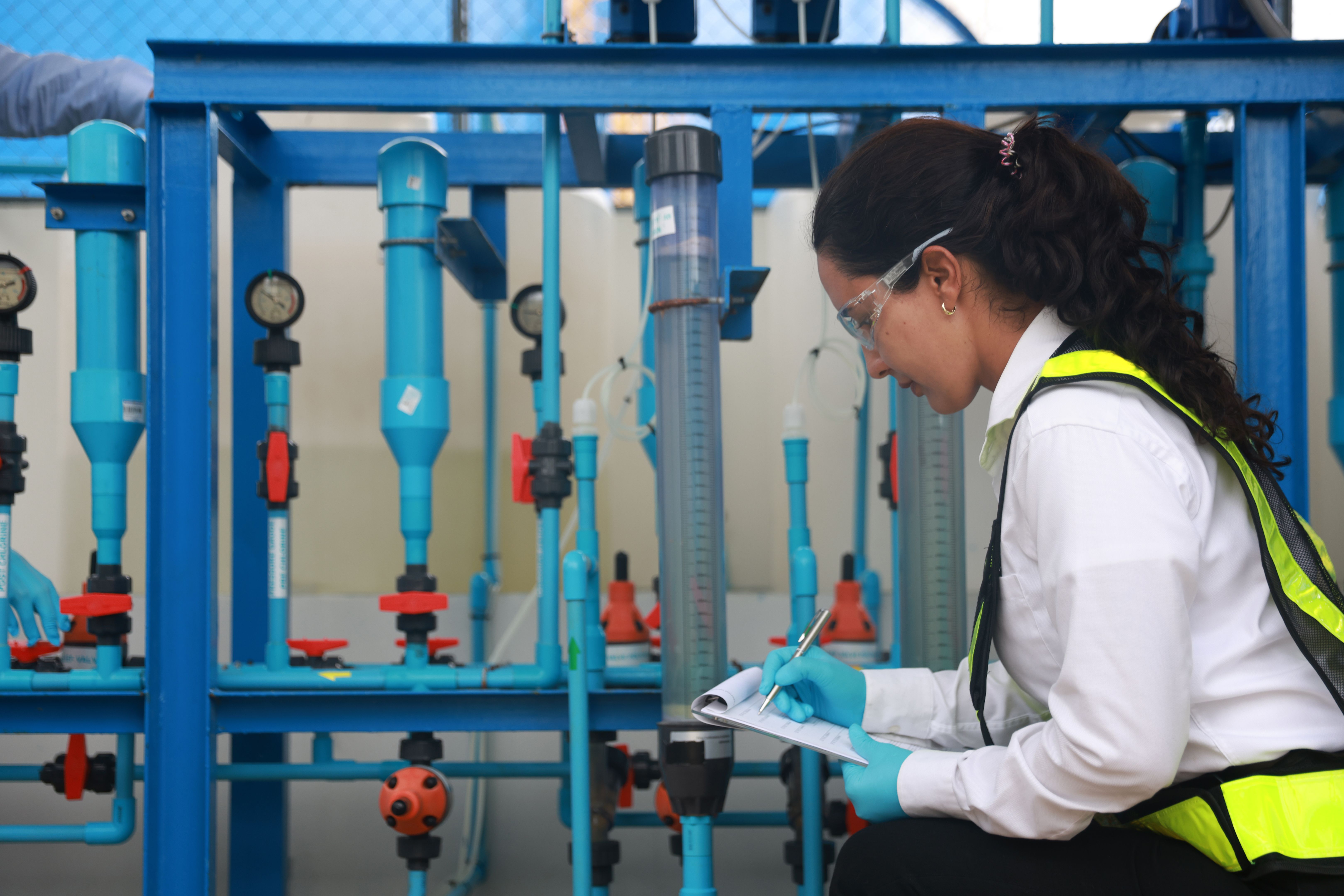 Two water treatment specialists, donned in safety vests and glasses, are conducting a quality inspection at water treatment process, industrial valve and piping Two water treatment specialists, donned in safety vests and glasses, are conducting a quality inspection at water treatment process, industrial valve and piping