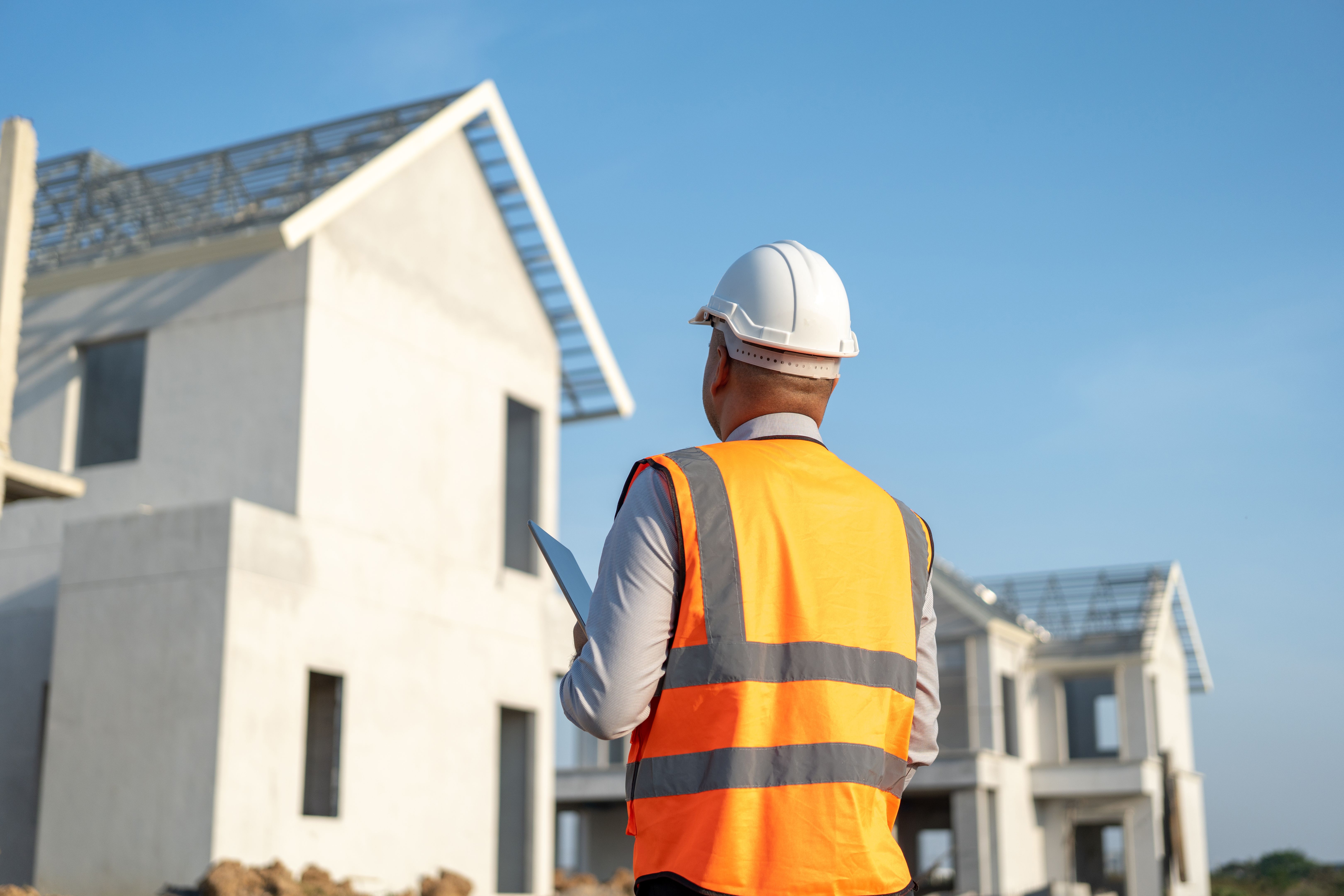 Confident asian engineer man Using tablet for checking and maintenance to inspection at modern home building construction. Architect working with white safety helmet in construction site