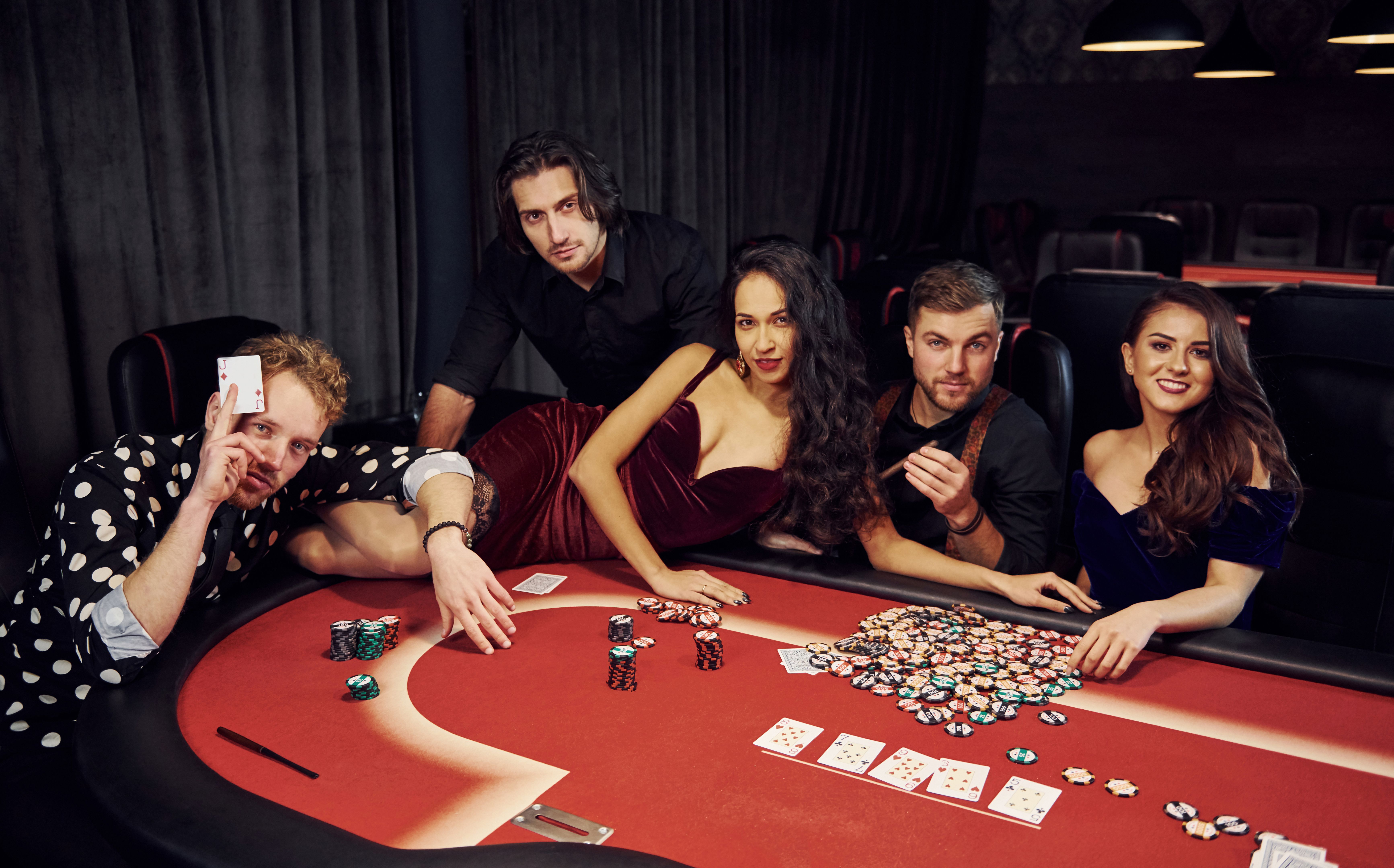 Woman lying down on table. Group of elegant young people that playing poker in casino together Woman lying down on table. Group of elegant young people that playing poker in casino together