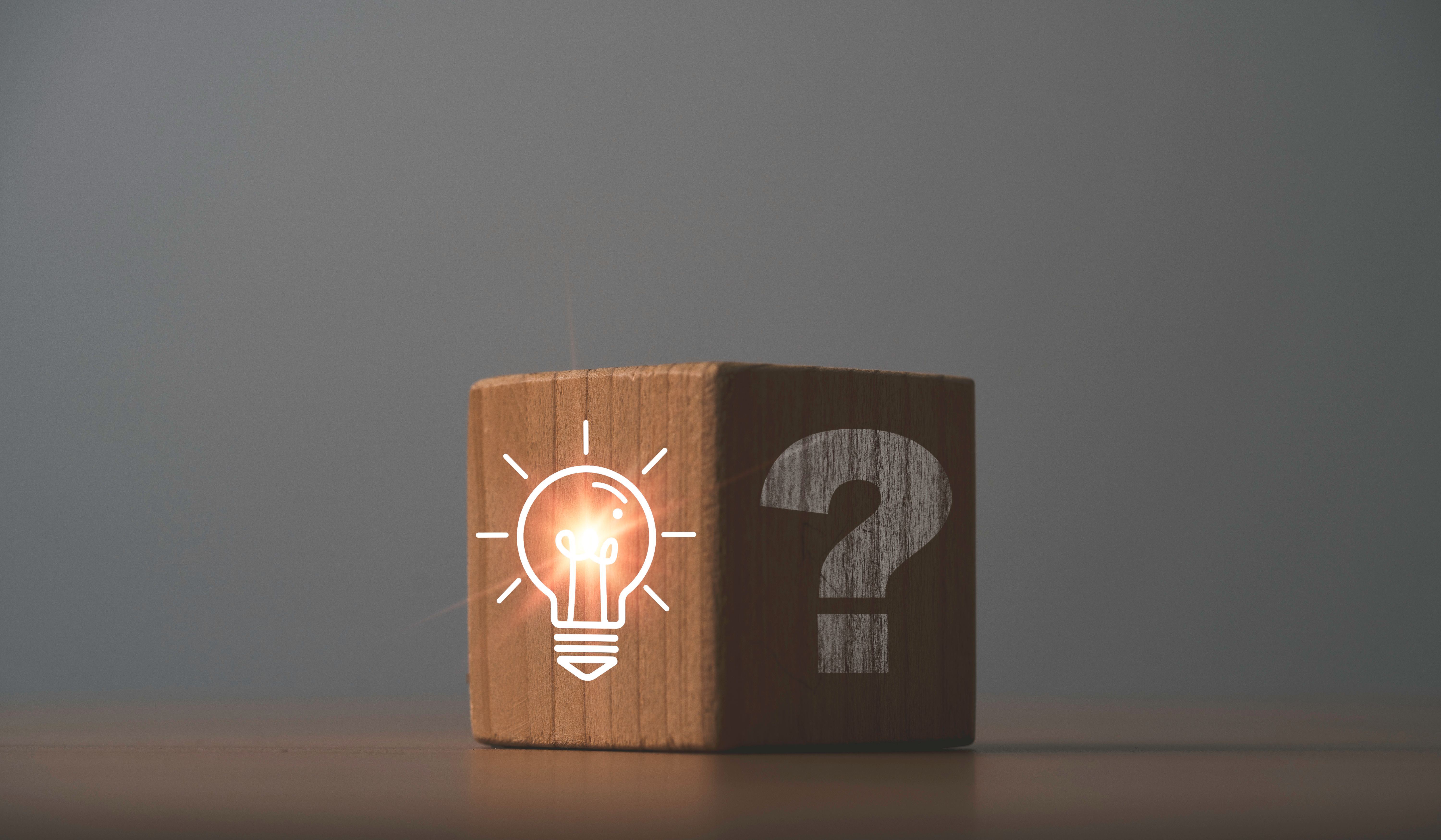 Glowing lightbulb on bright side and question mark on dark side of wooden block cube for problem solving solution and curative thinking idea innovation concept.