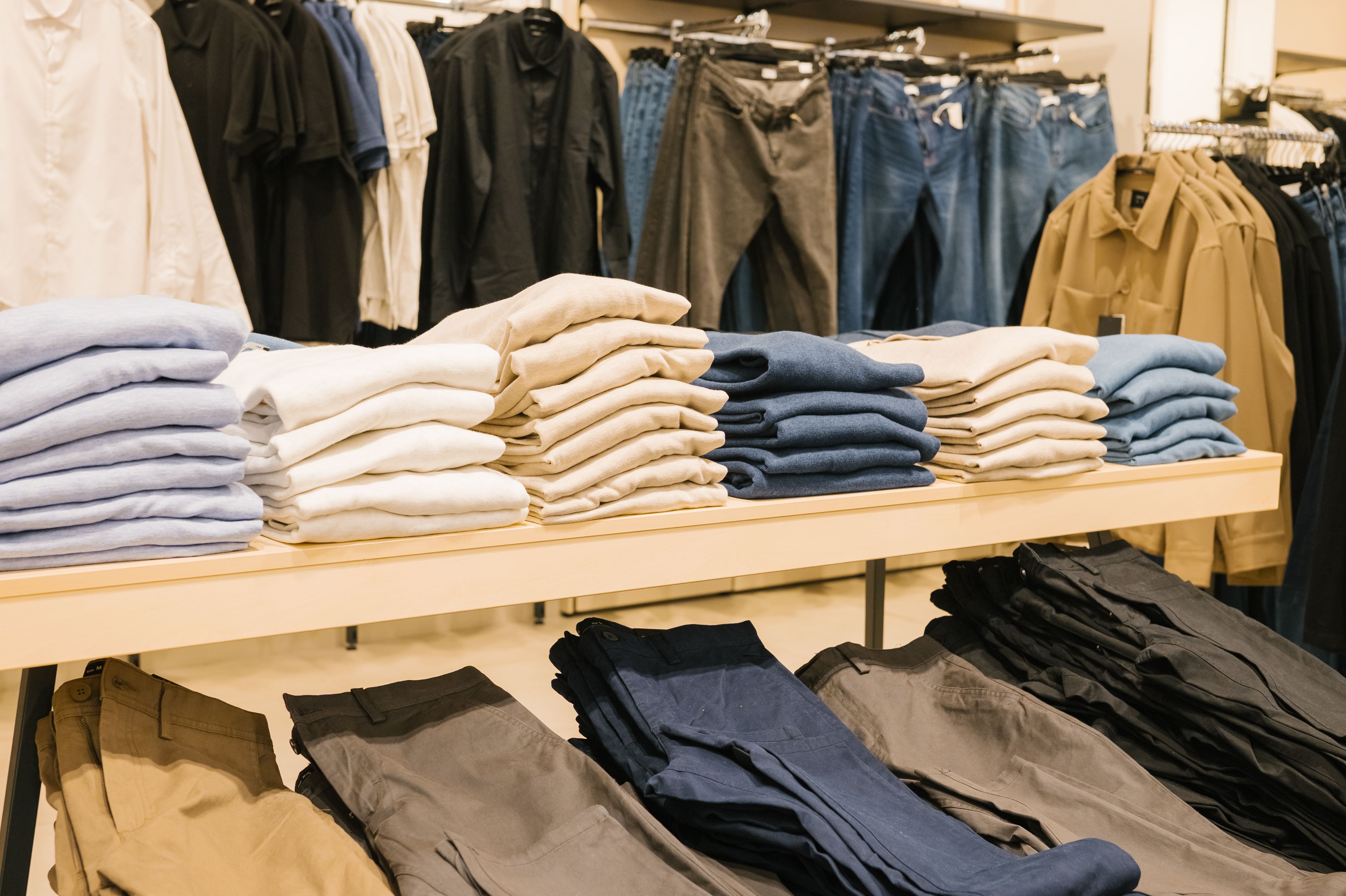 Casual clothing display in retail store with folded shirts and pants. National Thrift Shop Day