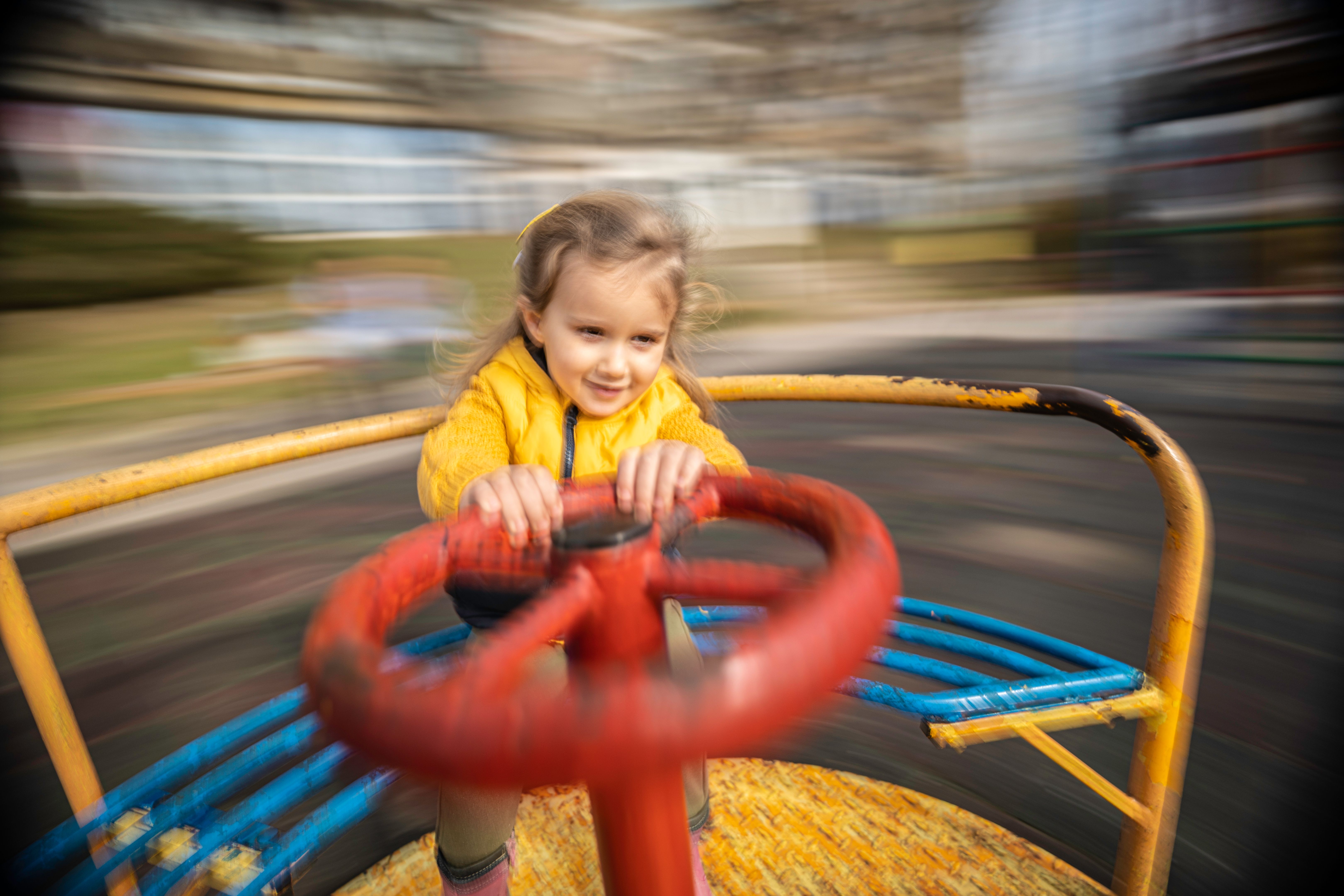 Happy Girl Spins on Merry-Go-Round on Playground in Spring.