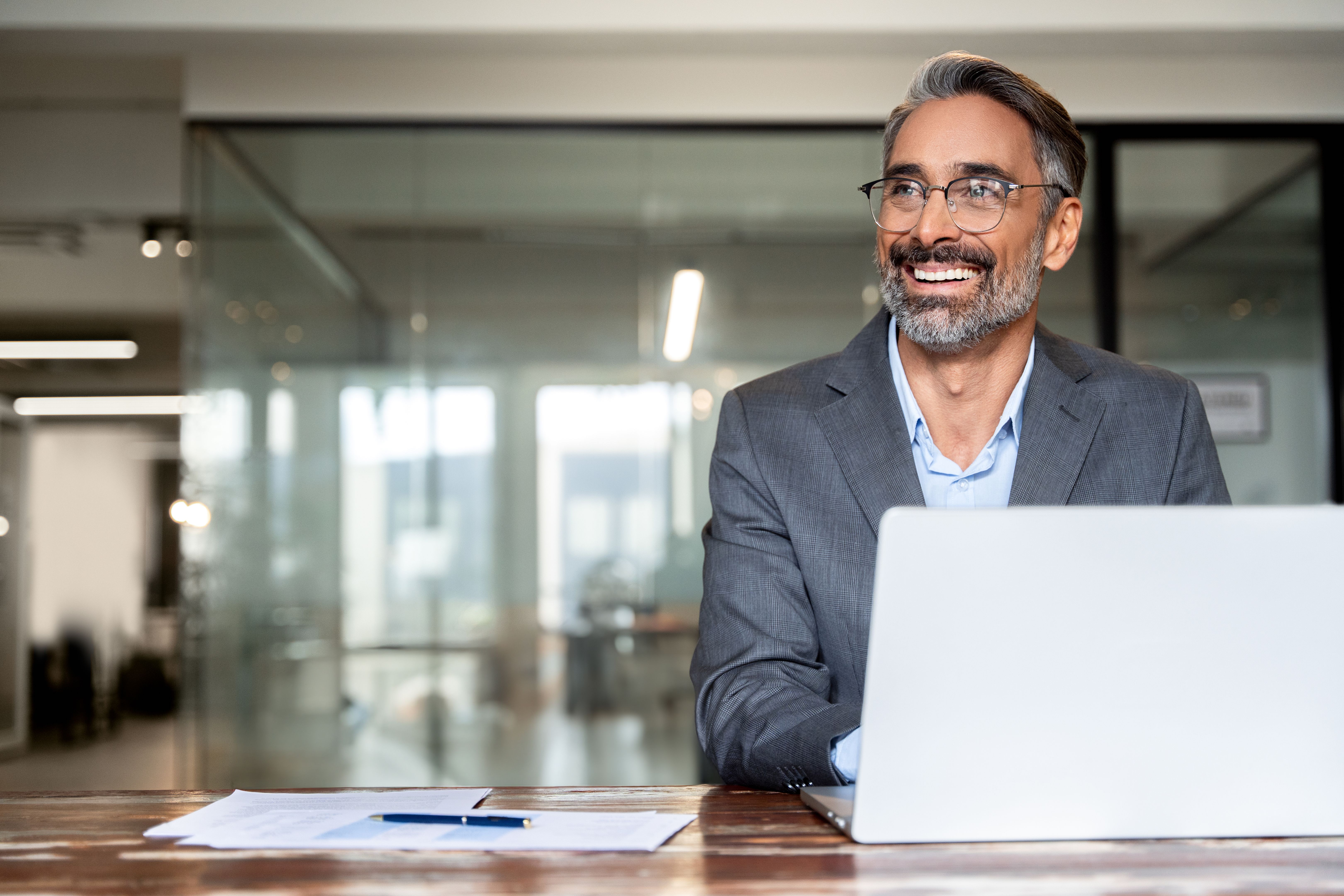 Portrait d’un homme d’affaires indien ou latin mature pdg trader utilisant un ordinateur portable, dactylographiant, travaillant dans un bureau moderne. Hispanique d’âge moyen souriant bel entrepreneur homme d’affaires regardant de côté, rêvant