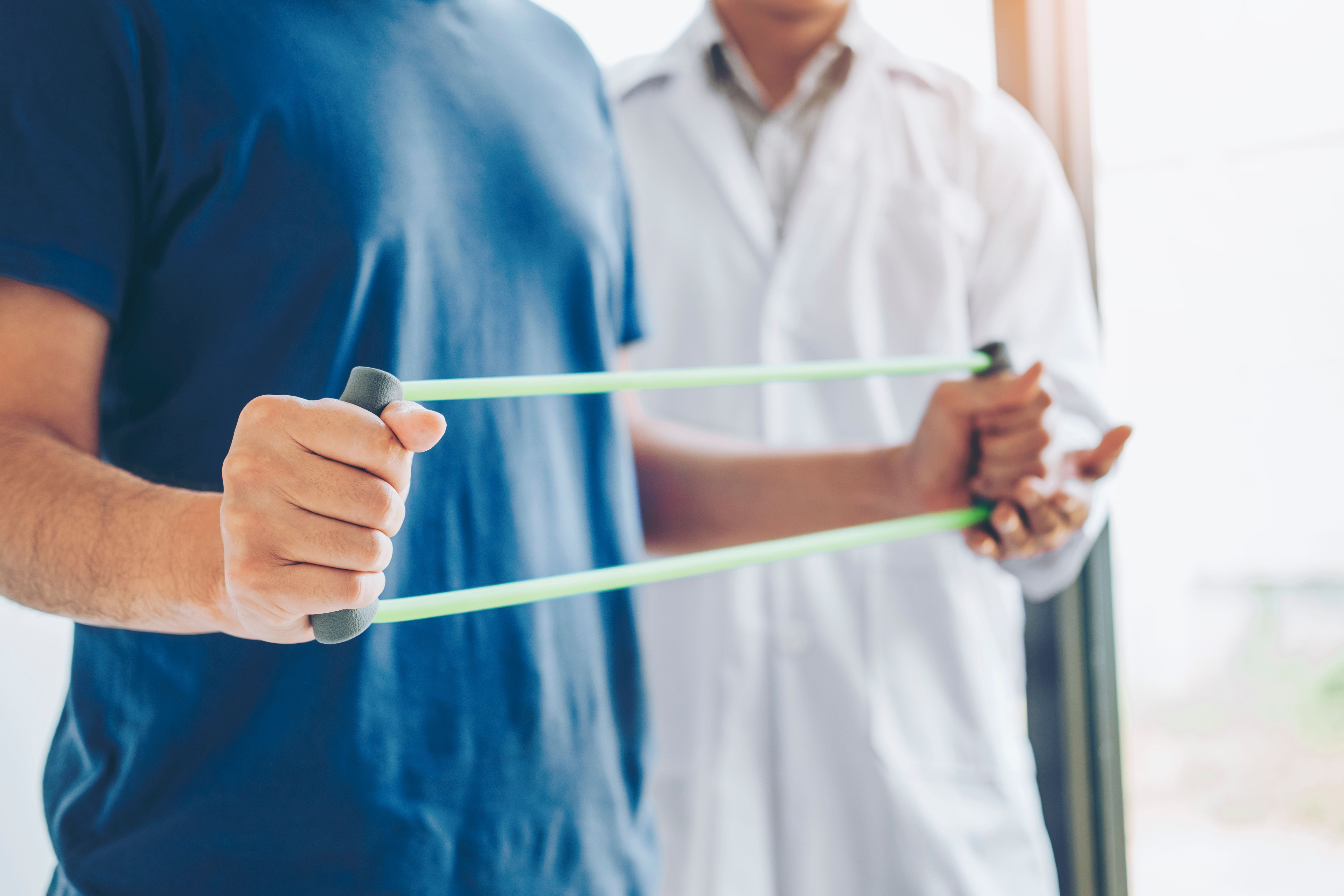 Physiotherapist man giving resistance band exercise treatment About Chest muscles and Shoulder of athlete male patient Physical therapy concept