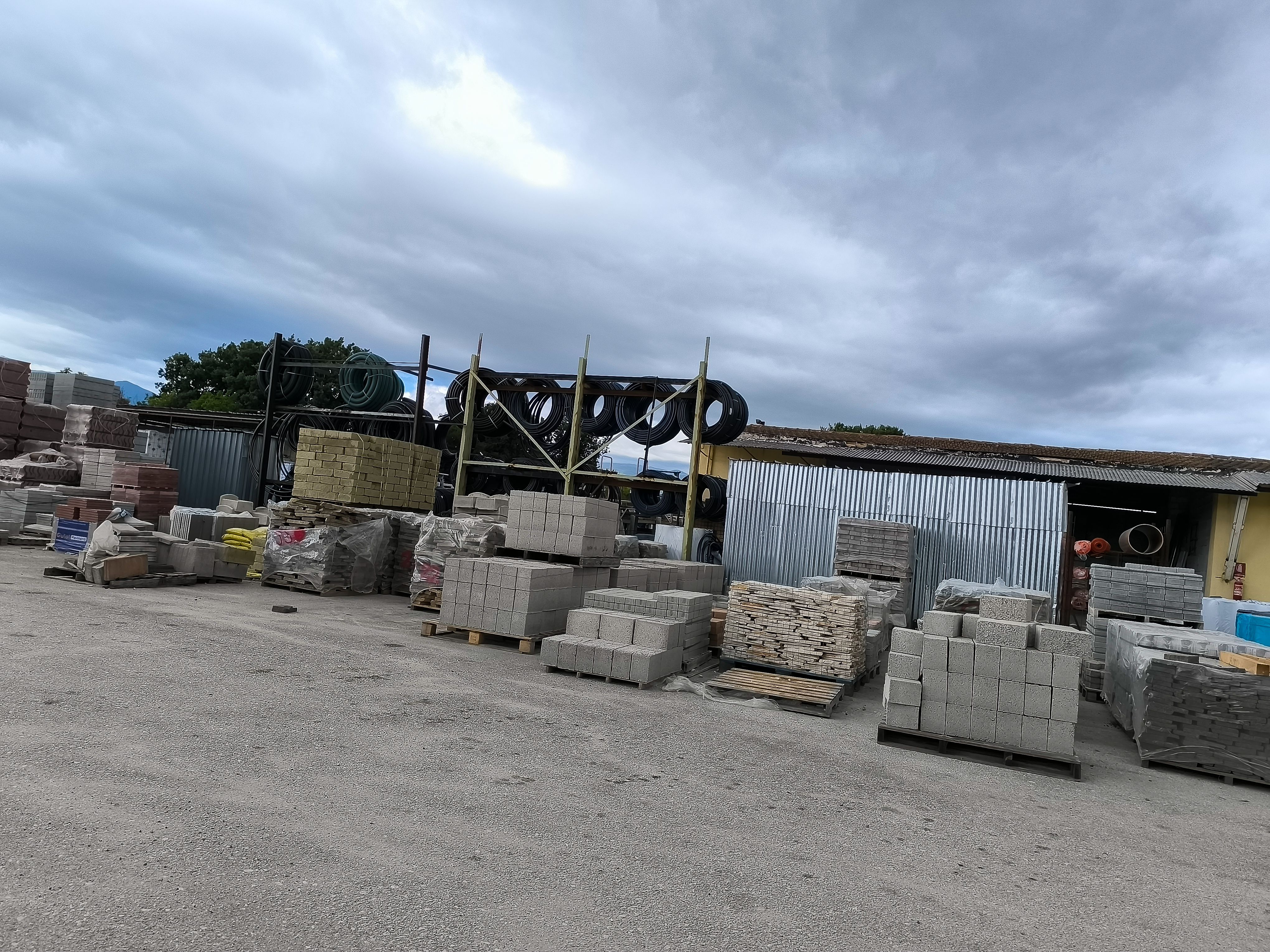 Construction materials yard bustling with activity under a cloudy sky in a rural area