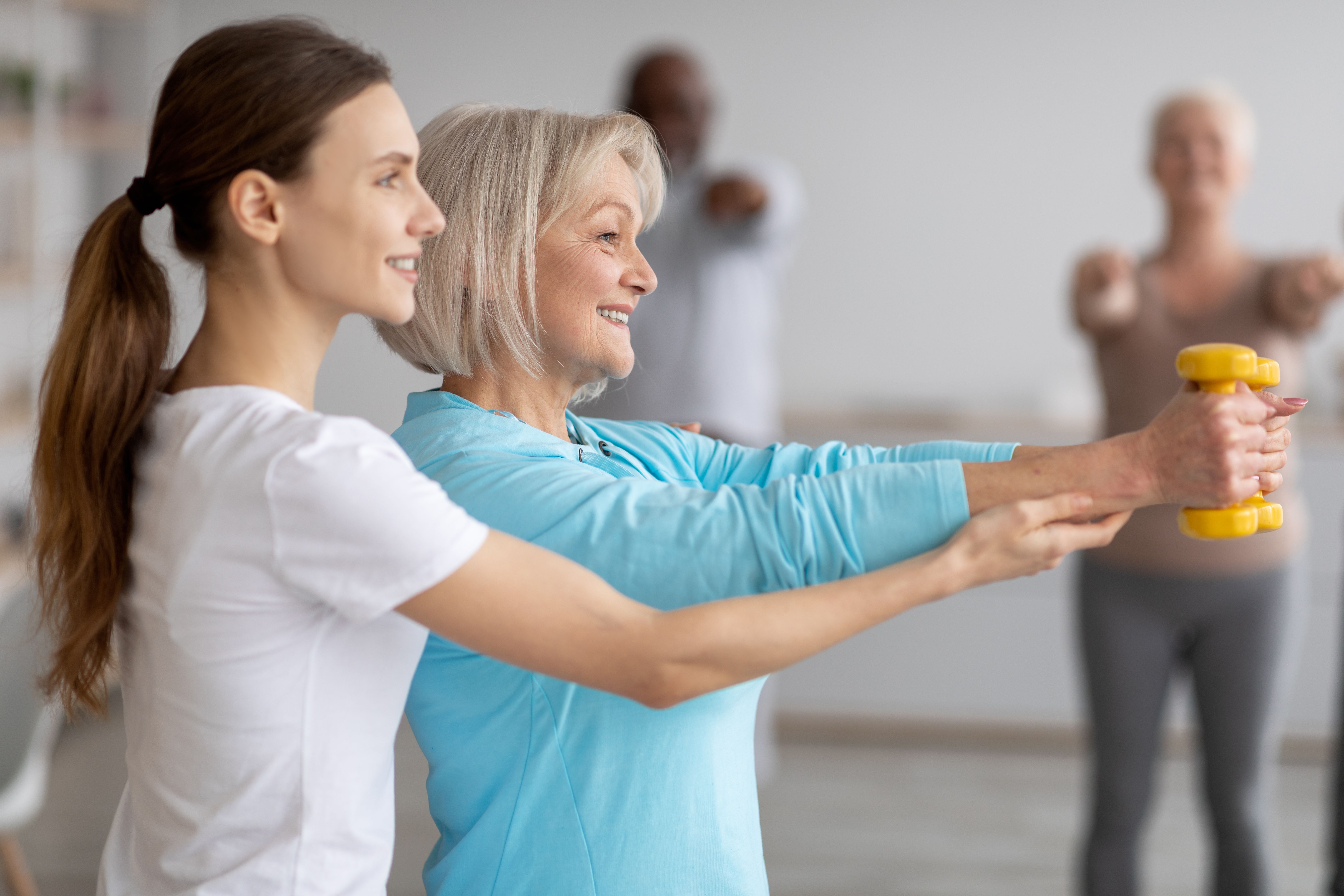 Side view of fitness coach helping senior woman while exercising