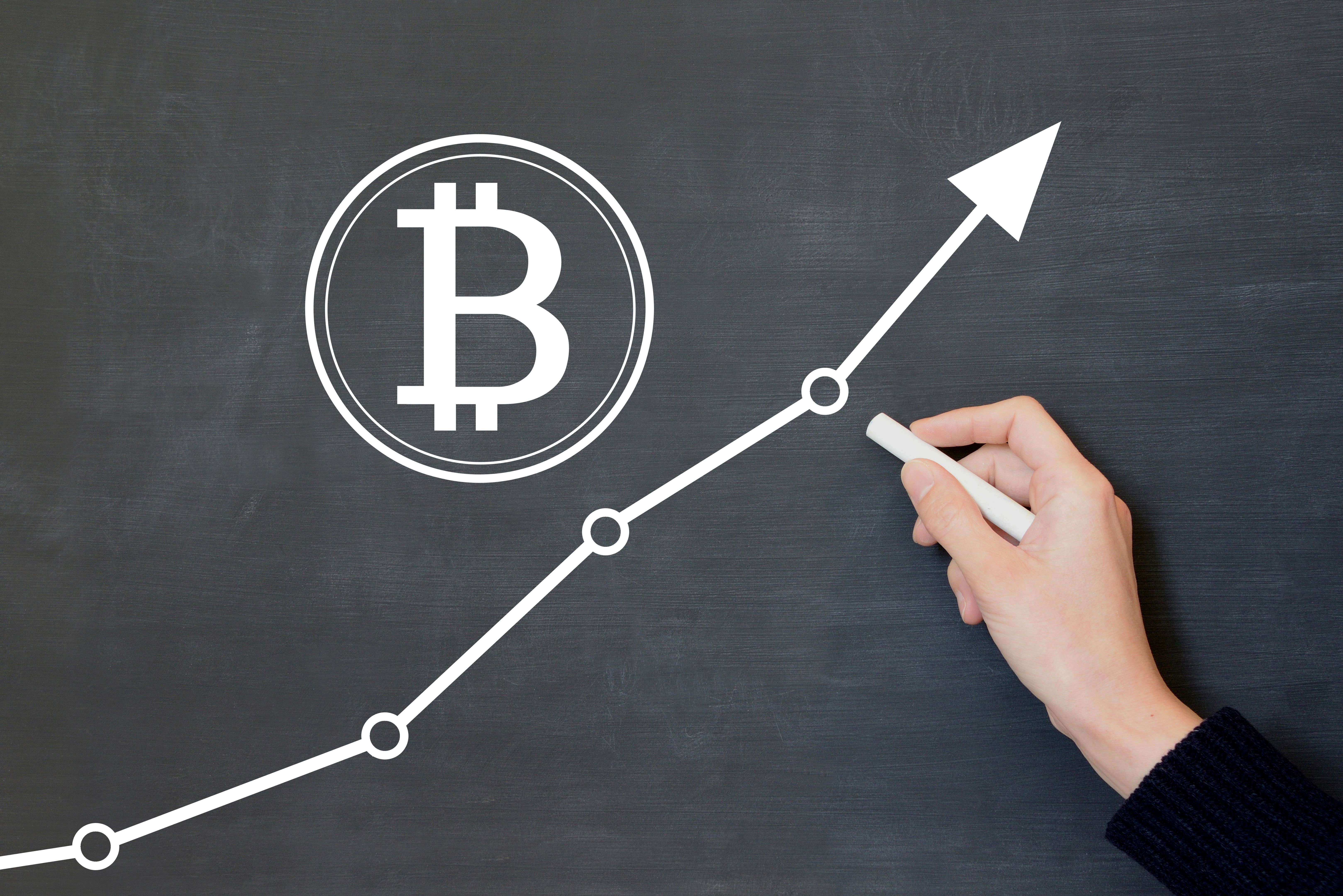 Human's hand drawing bitcoin sign and upward arrow