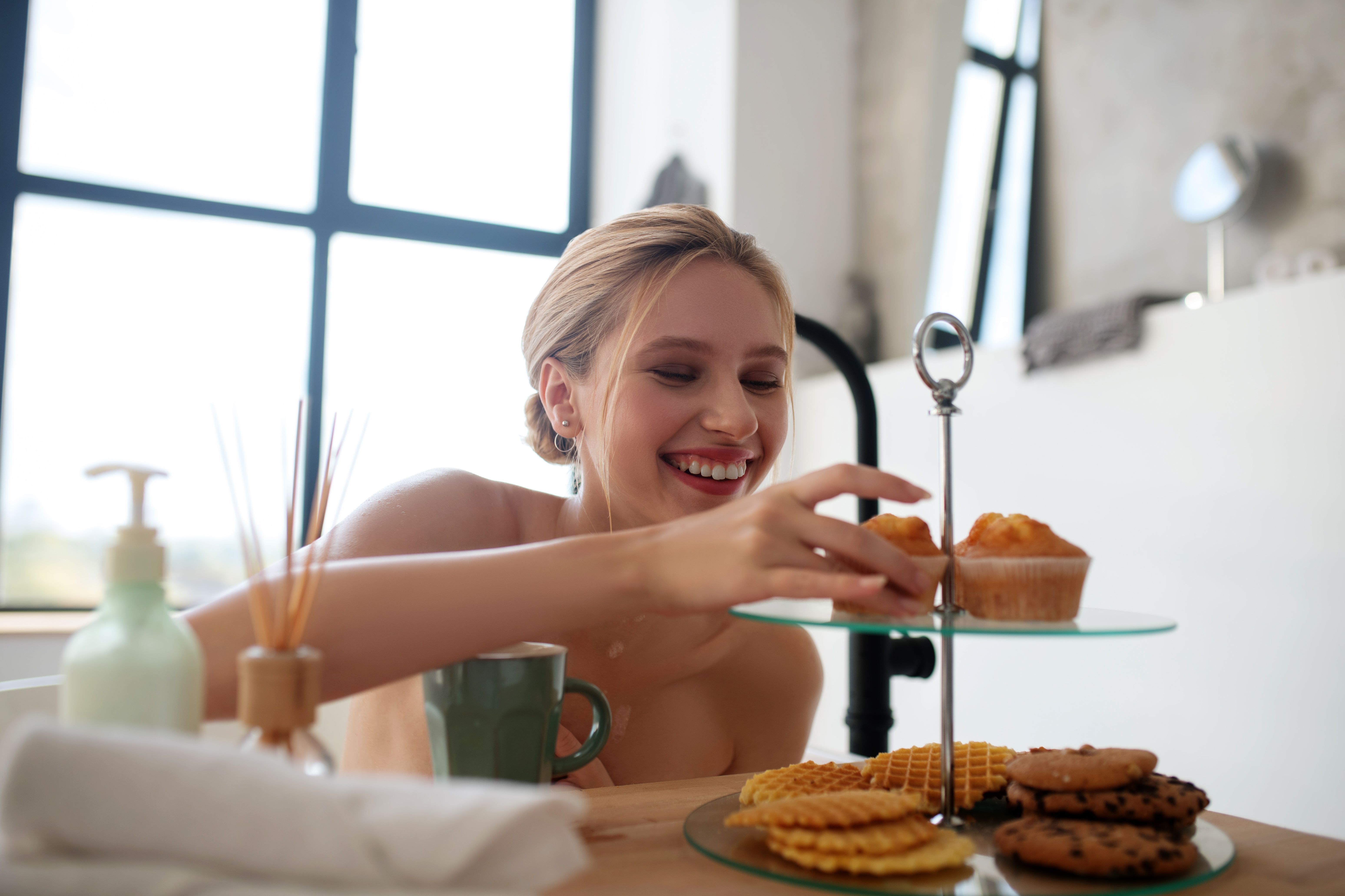 Smiling woman taking cupcake while sitting in bath Smiling woman taking cupcake while sitting in bath