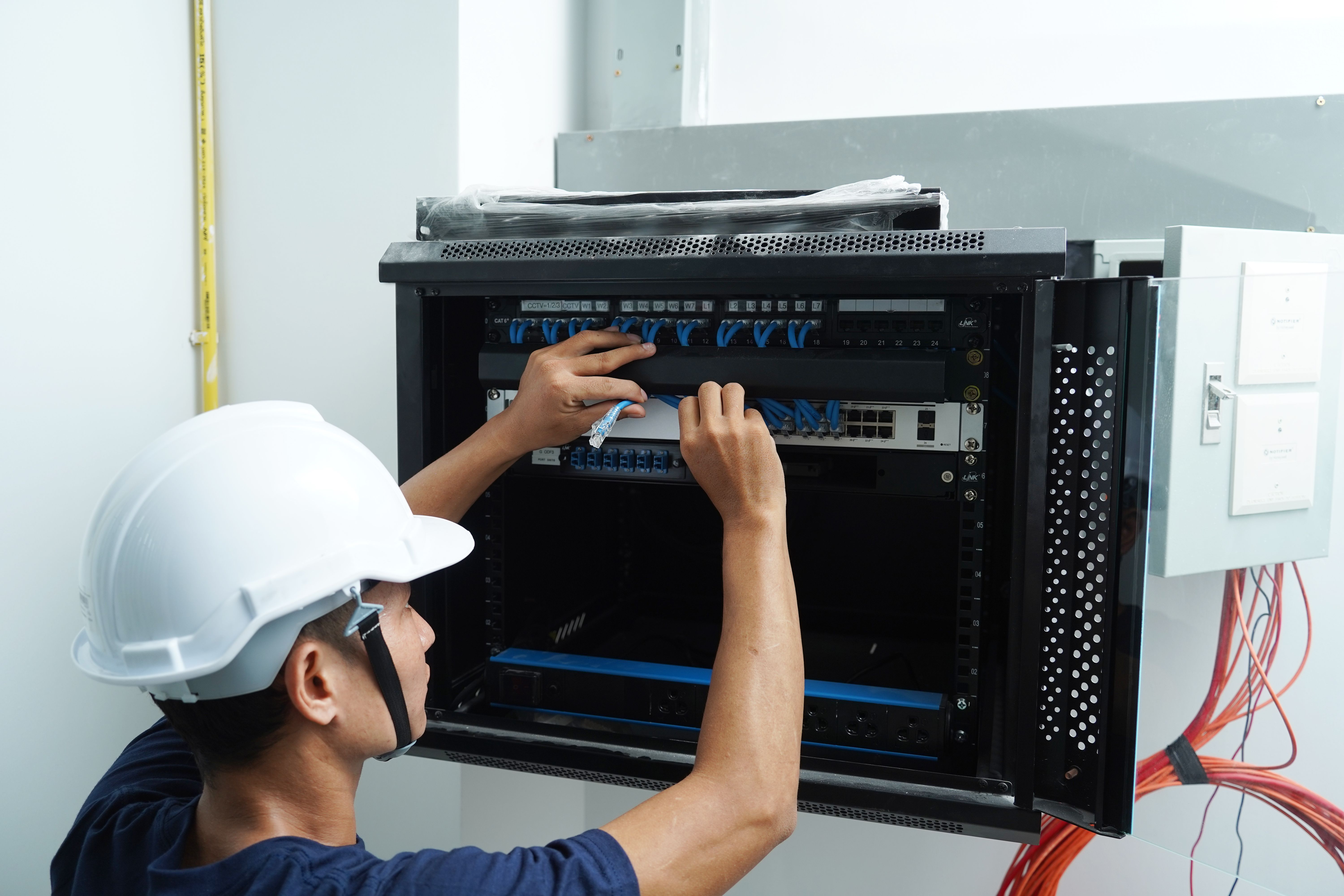 A maintenance technician works in a server room with a fiber optic hub