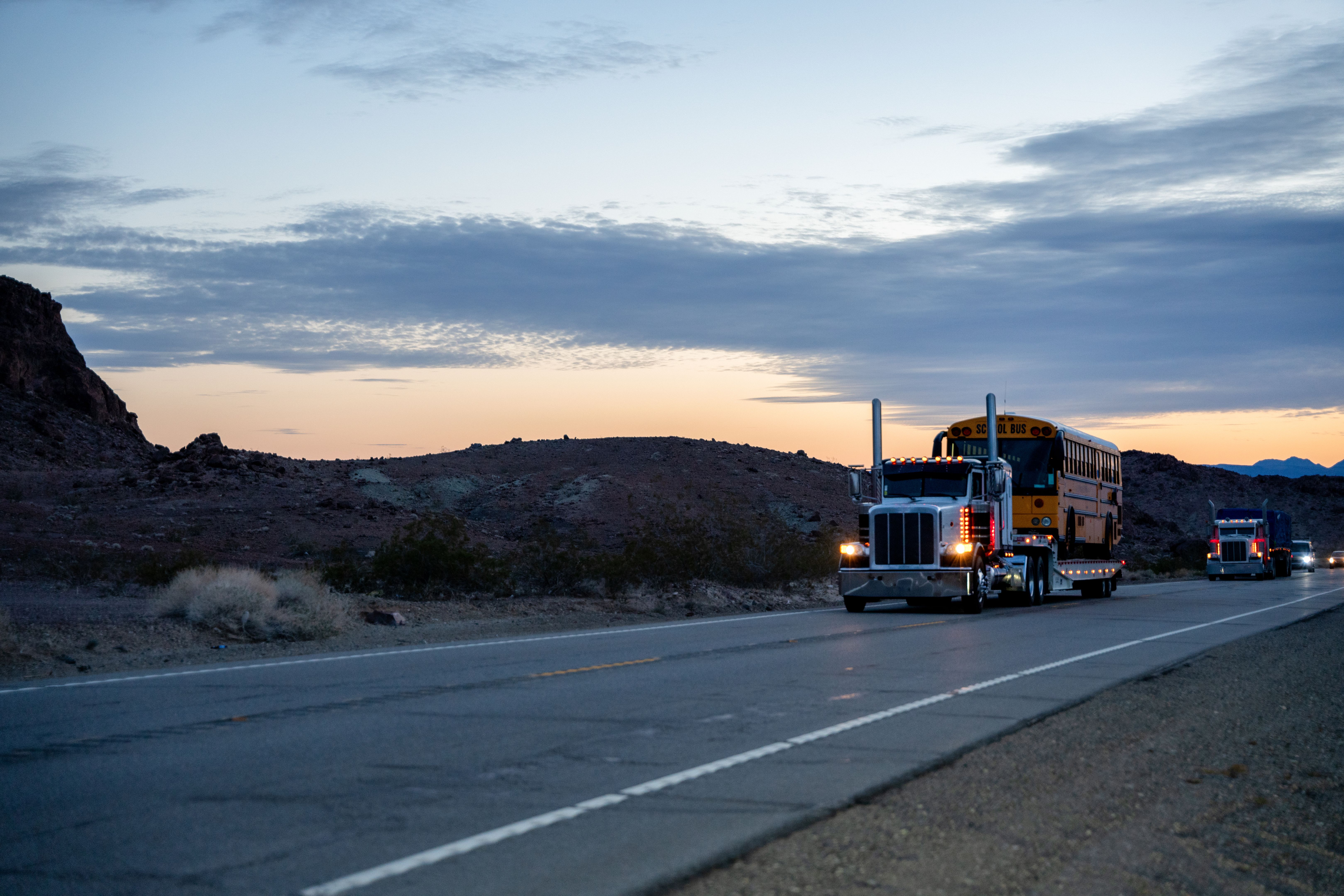 A Semi-Truck on a Two-Lane Highway Hauling a School Bus at Sunset