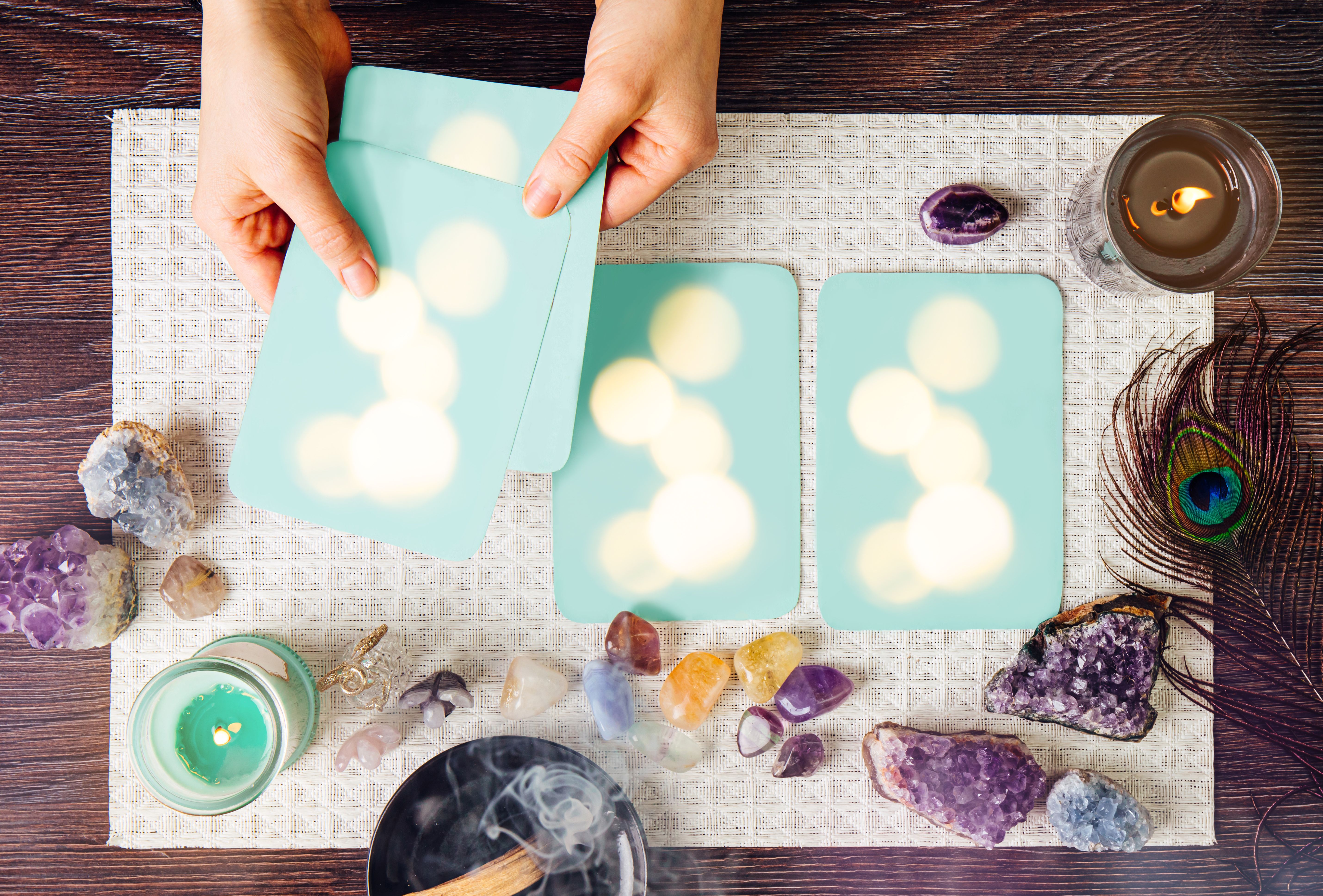 Deck with homemade divination Angel cards on white background, surrounded with semi precious stones crystals, candles burning. Selective focus on amethyst crystal angel figurine. Deck with homemade divination Angel cards on white background, surrounded with semi precious stones crystals, candles burning. Selective focus on amethyst crystal angel figurine.