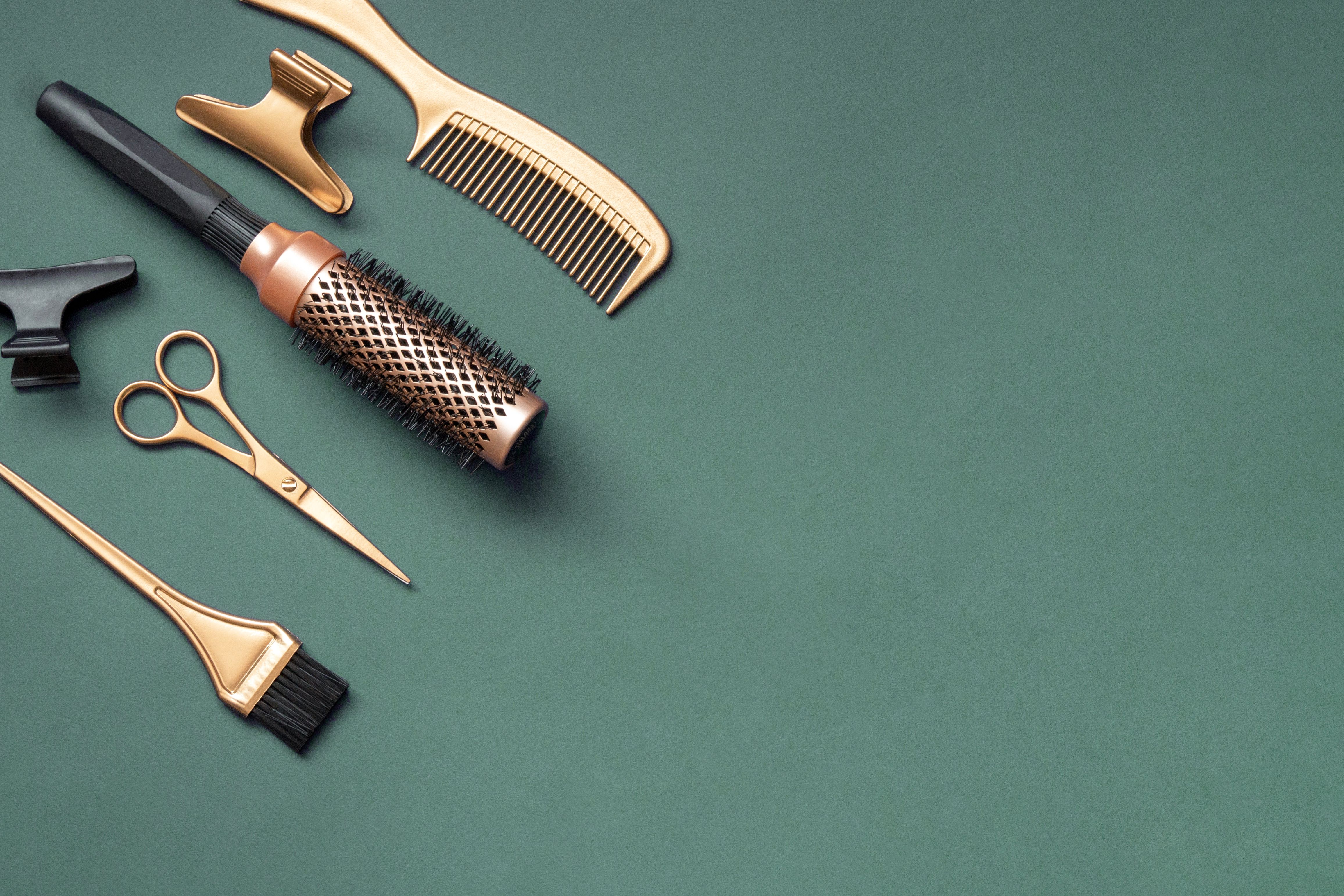 Golden hairdressing tools scissors combs on green background. Horizontal template with hair salon accessories and copy space.