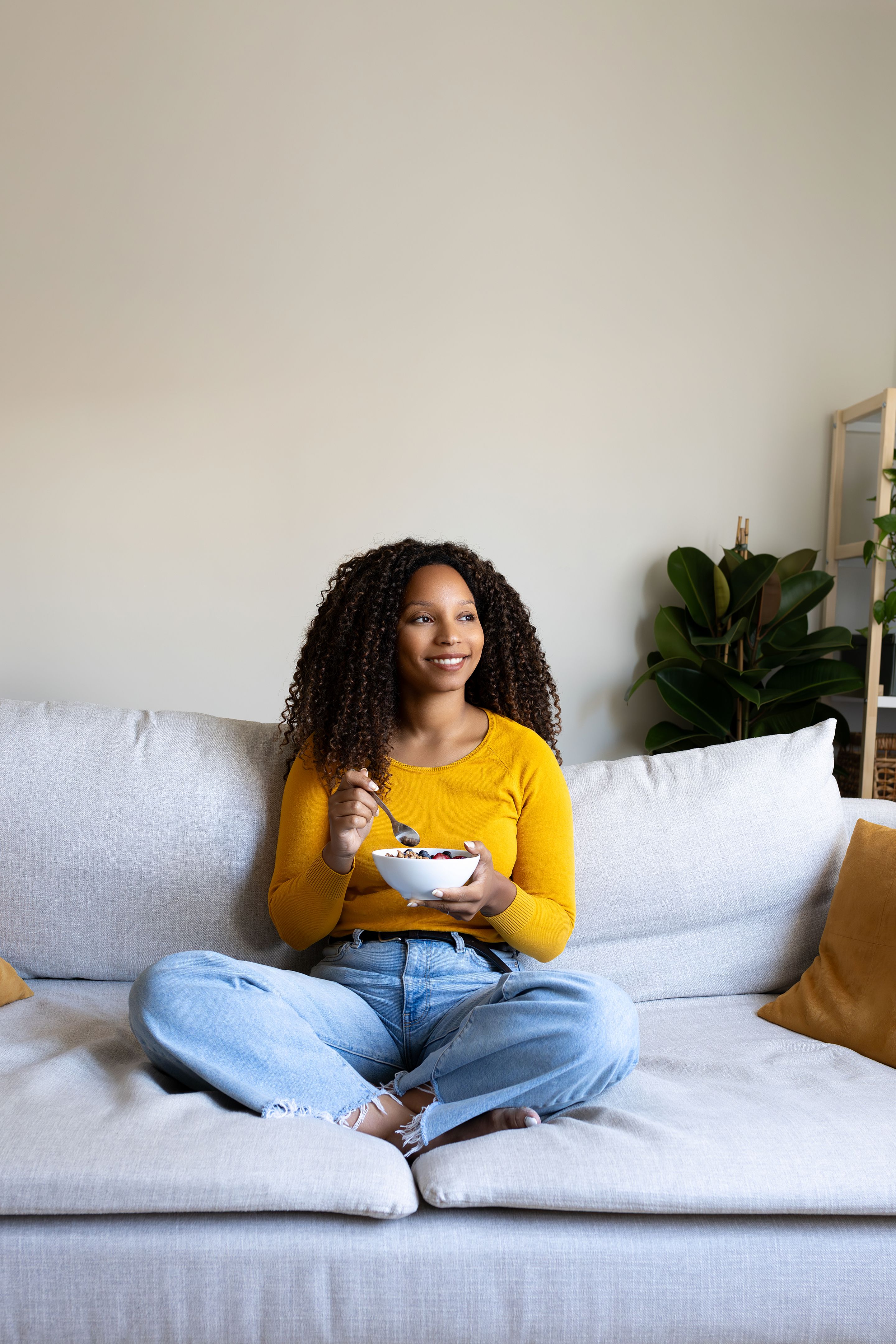 Relaxed Black woman eating breakfast sitting on the couch at home cozy living room. Vertical image, Copy space. Relaxed Black woman eating breakfast sitting on the couch at home cozy living room. Vertical image, Copy space.