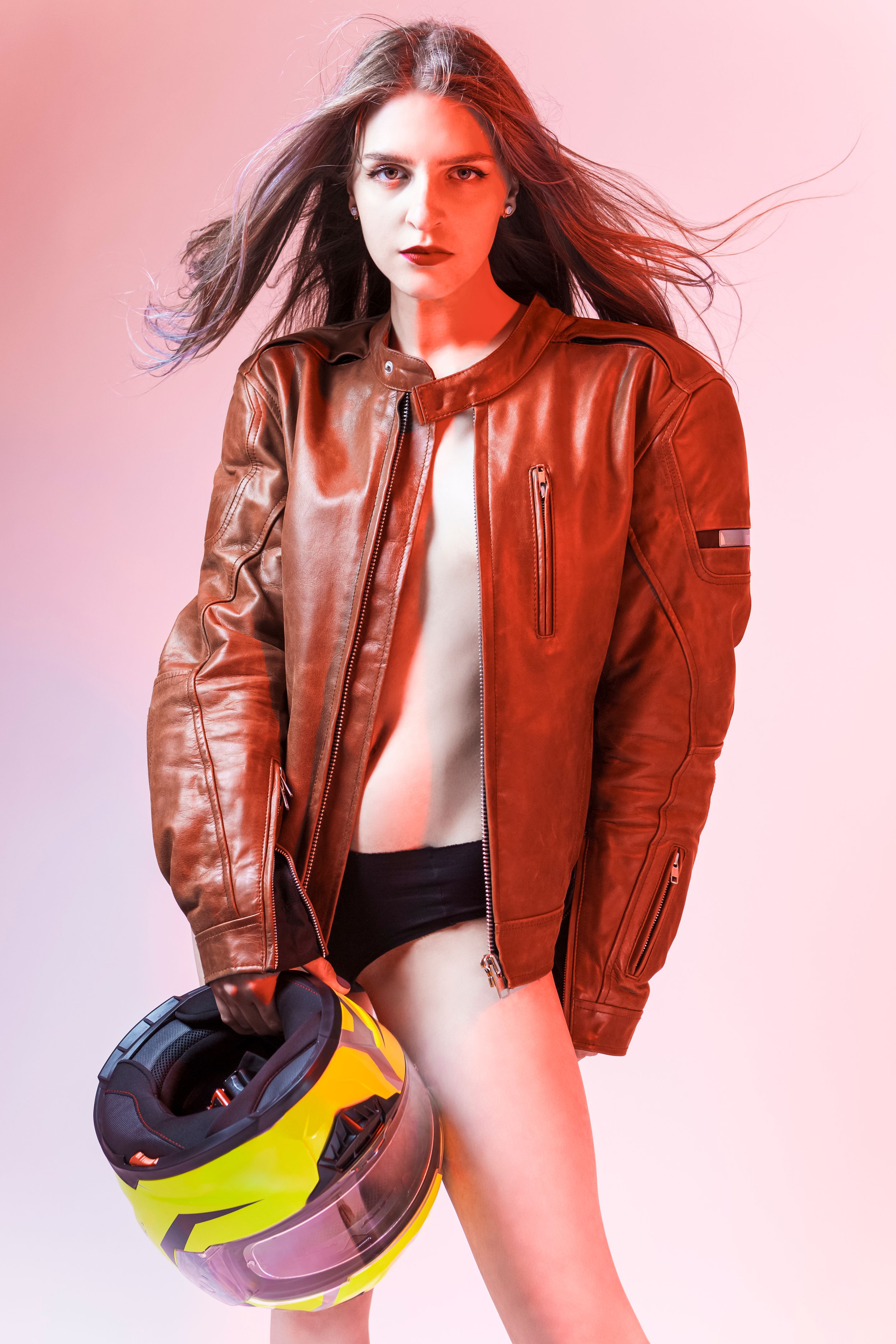 Natural Portrait of Sexy Caucasian Female Motorcyclist Posing In Leather Protective Jacket And Helmet Over Yellow Background.