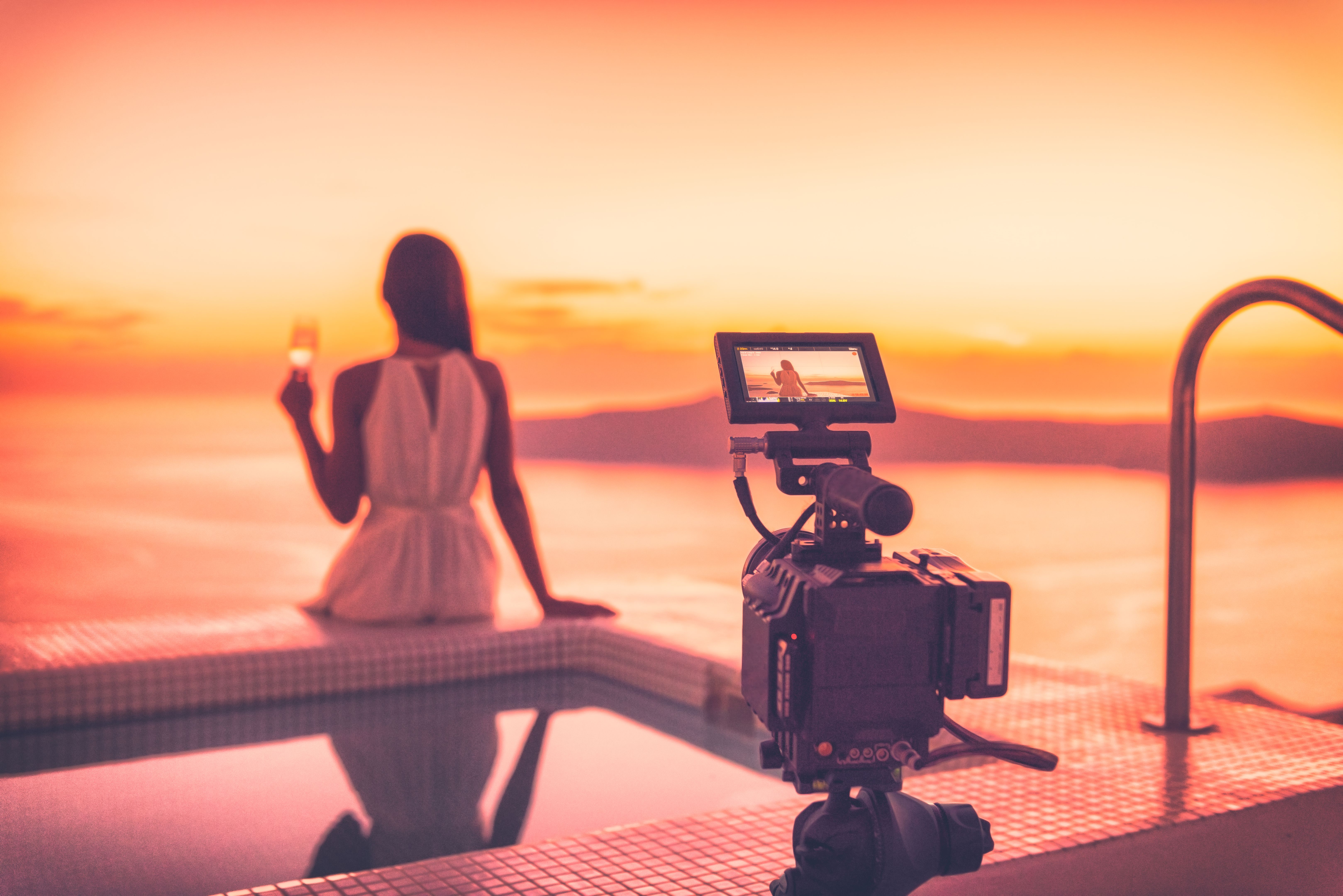 Videography behind the scene video camera shooting movie at sunset beach resort hotel filming actress woman acting, luxury travel. Professional videography equipment shooting outdoor at sunset.