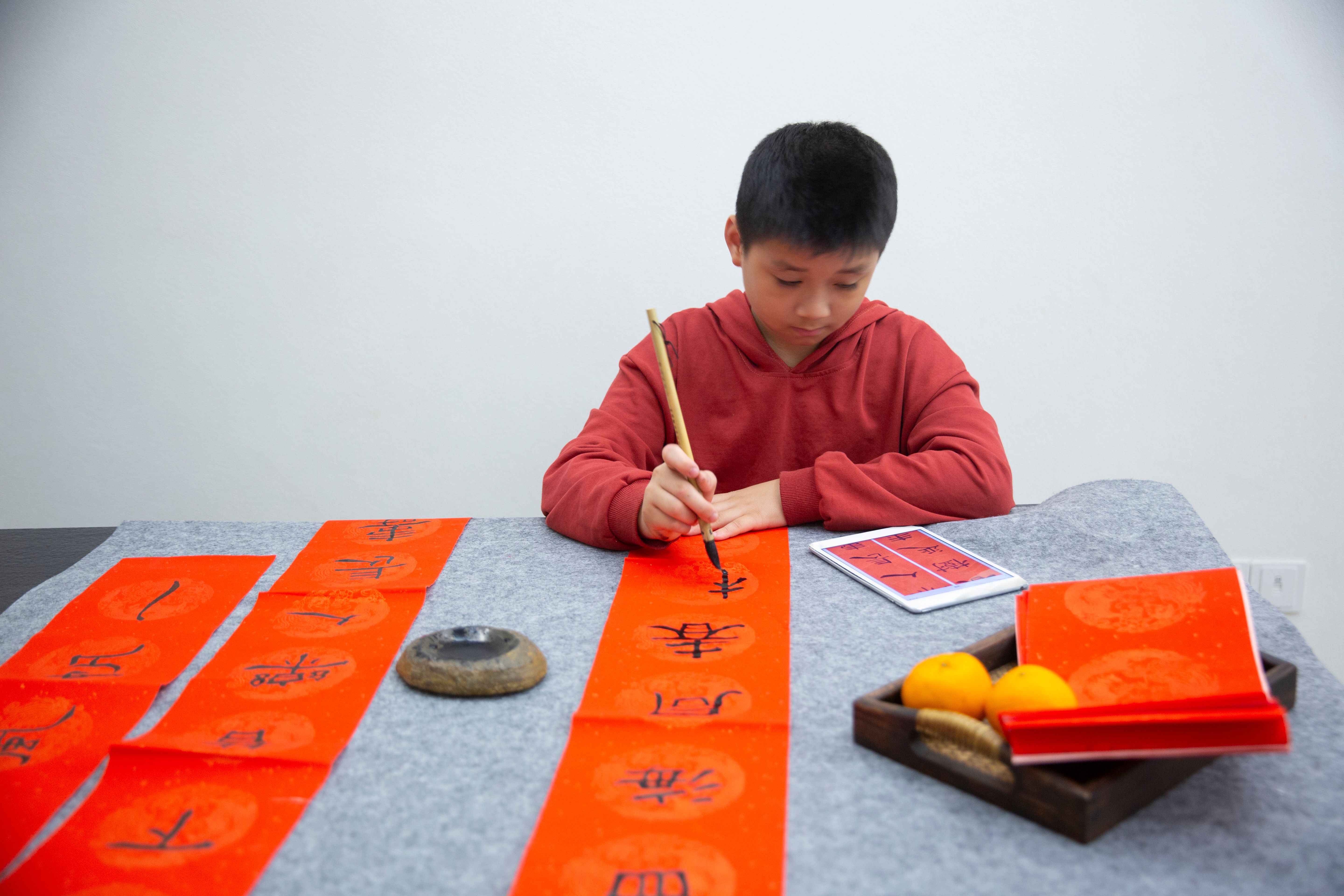 A cute Asian boy writes Chinese couplets with a brush at home