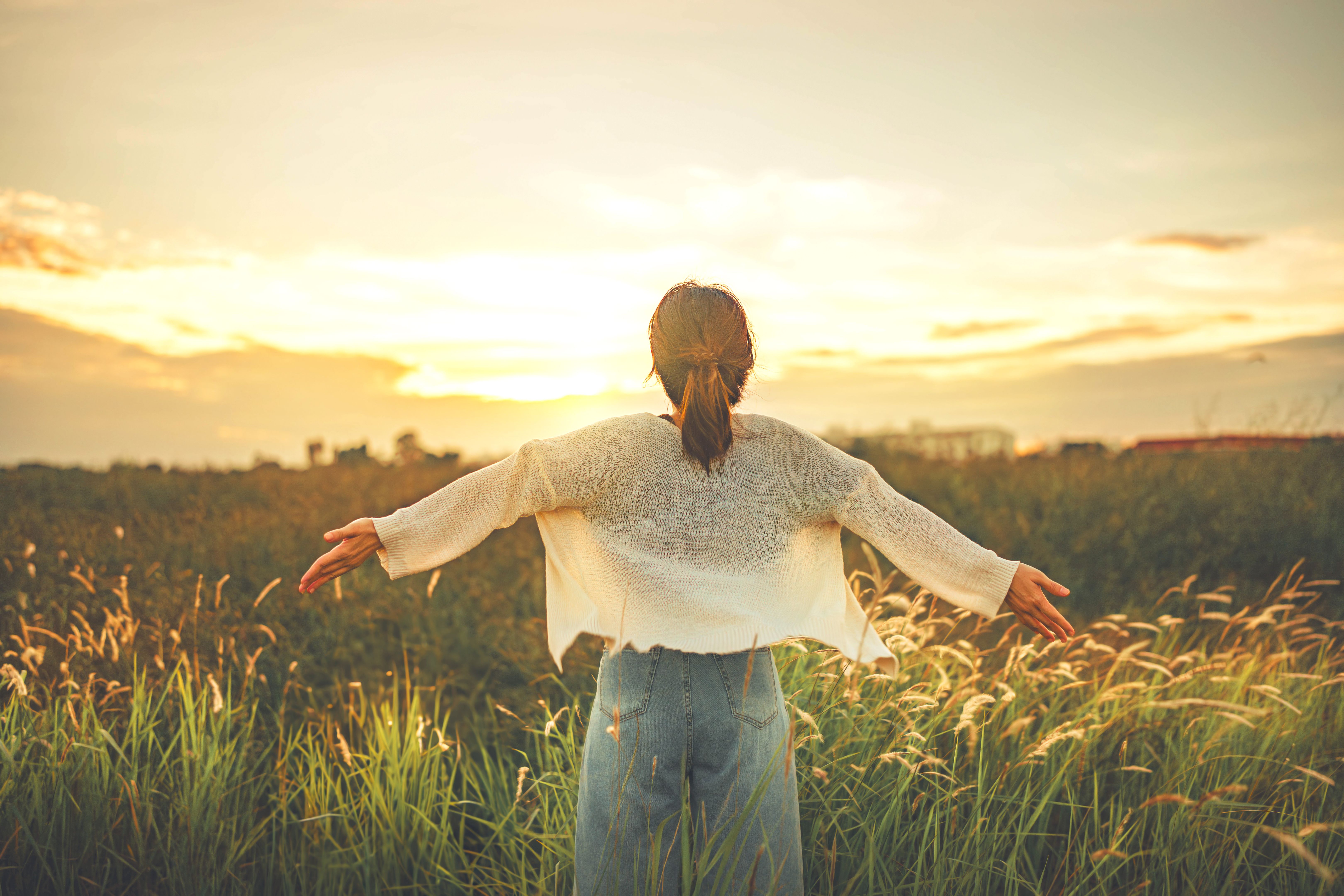 Happy woman with arms outstretched in the field with flowers in sunset. Freedom