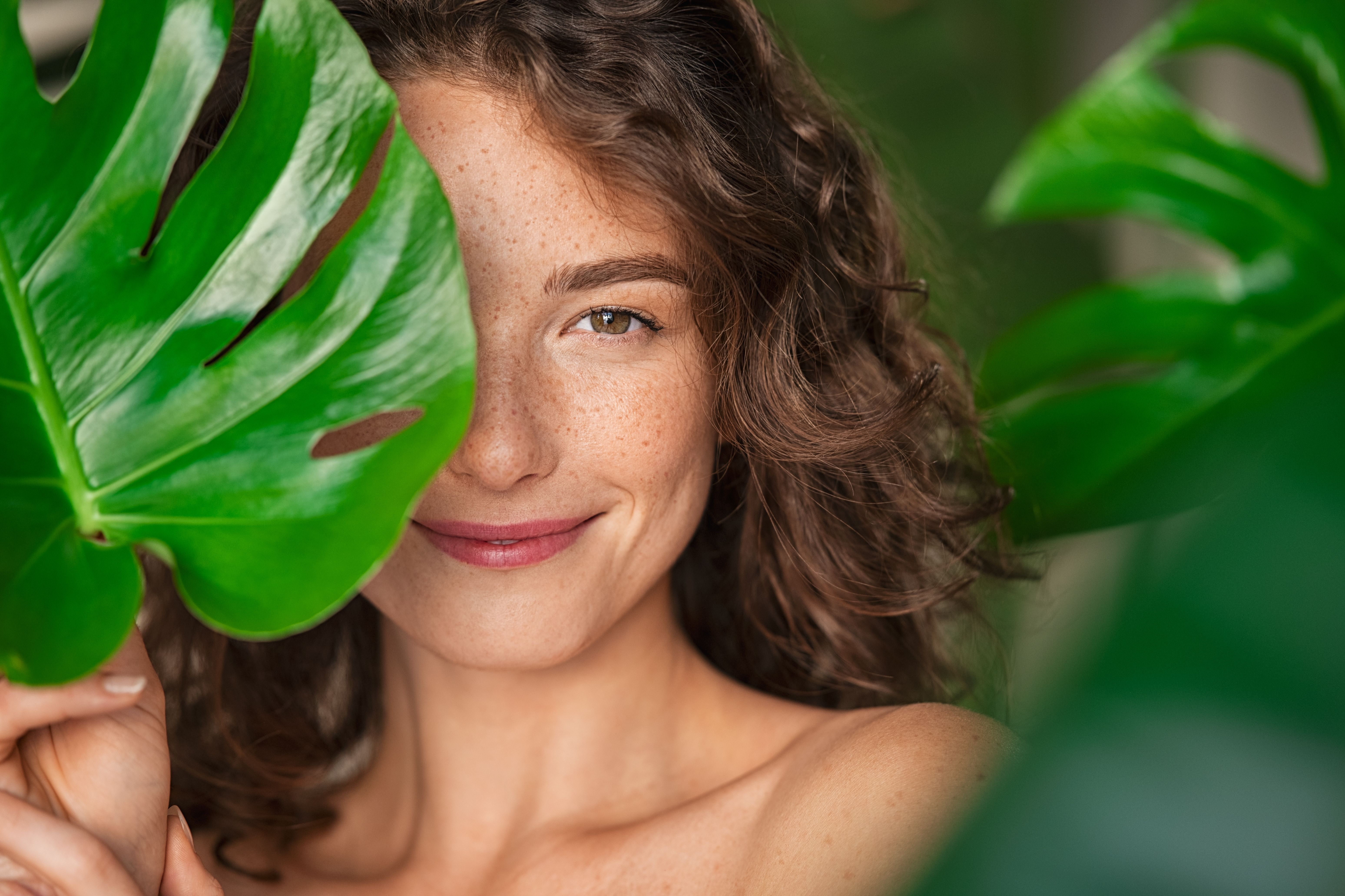 Beauty natural woman covering her face with tropical leaf Beauty natural woman covering her face with tropical leaf