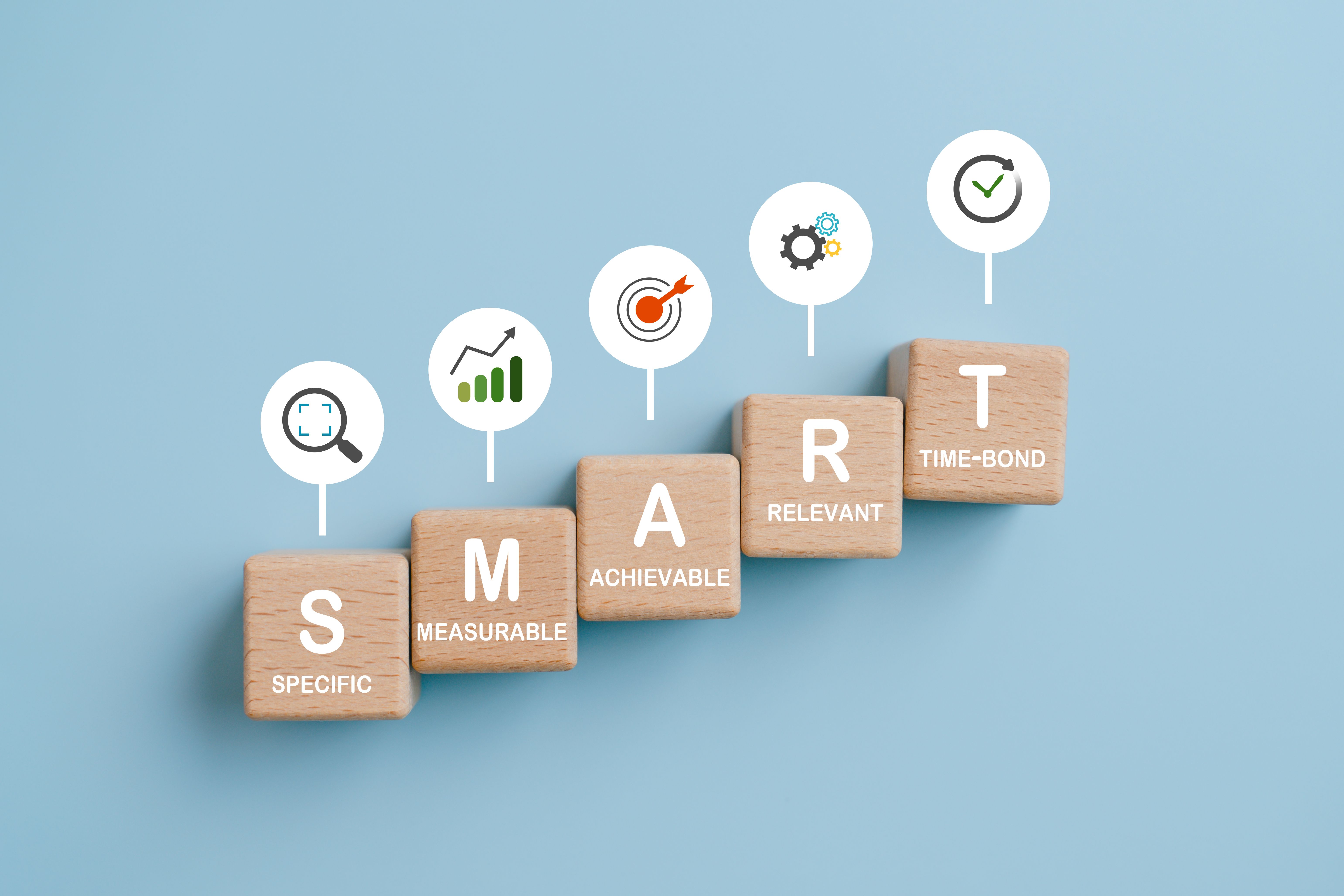 Smart goal for business strategy concept. specific, measurable, achievable, relevant and time-bound text on wooden block with icons on blue background