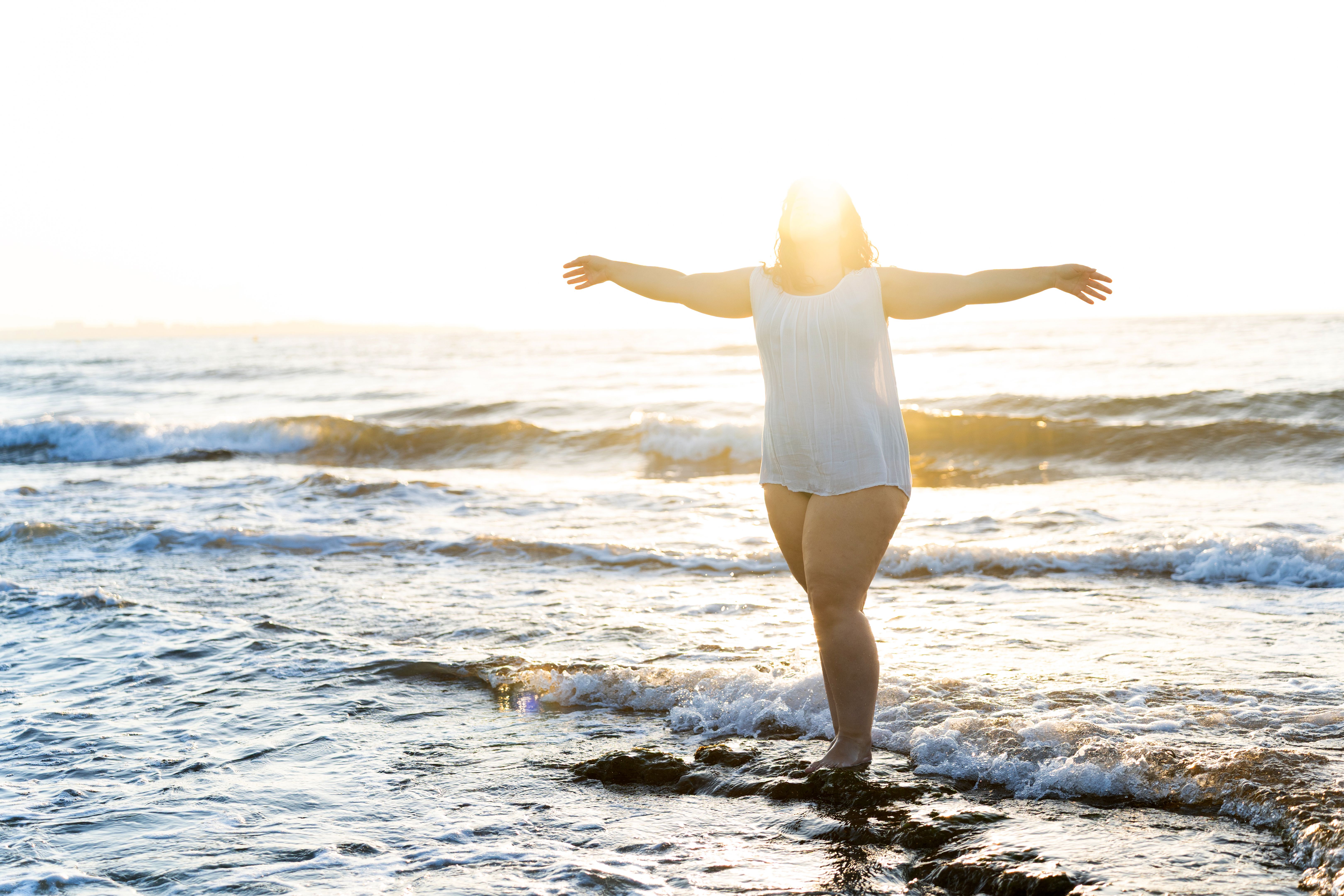 Curvy woman enjoying freedom on the beach at sunset