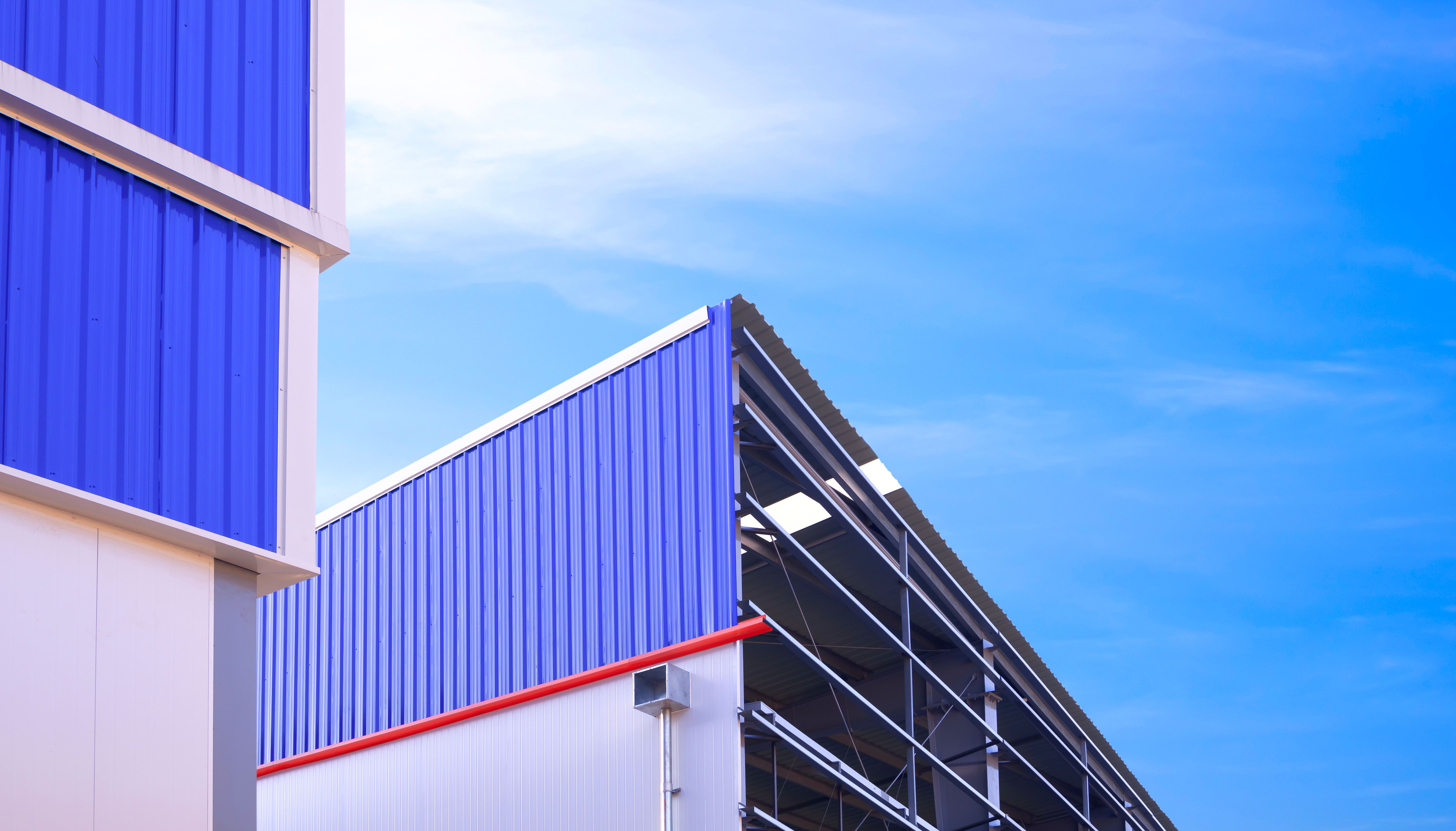Warehouse industrial factory building framework with corrugated aluminum on metal wall structure in under construction against blue sky background