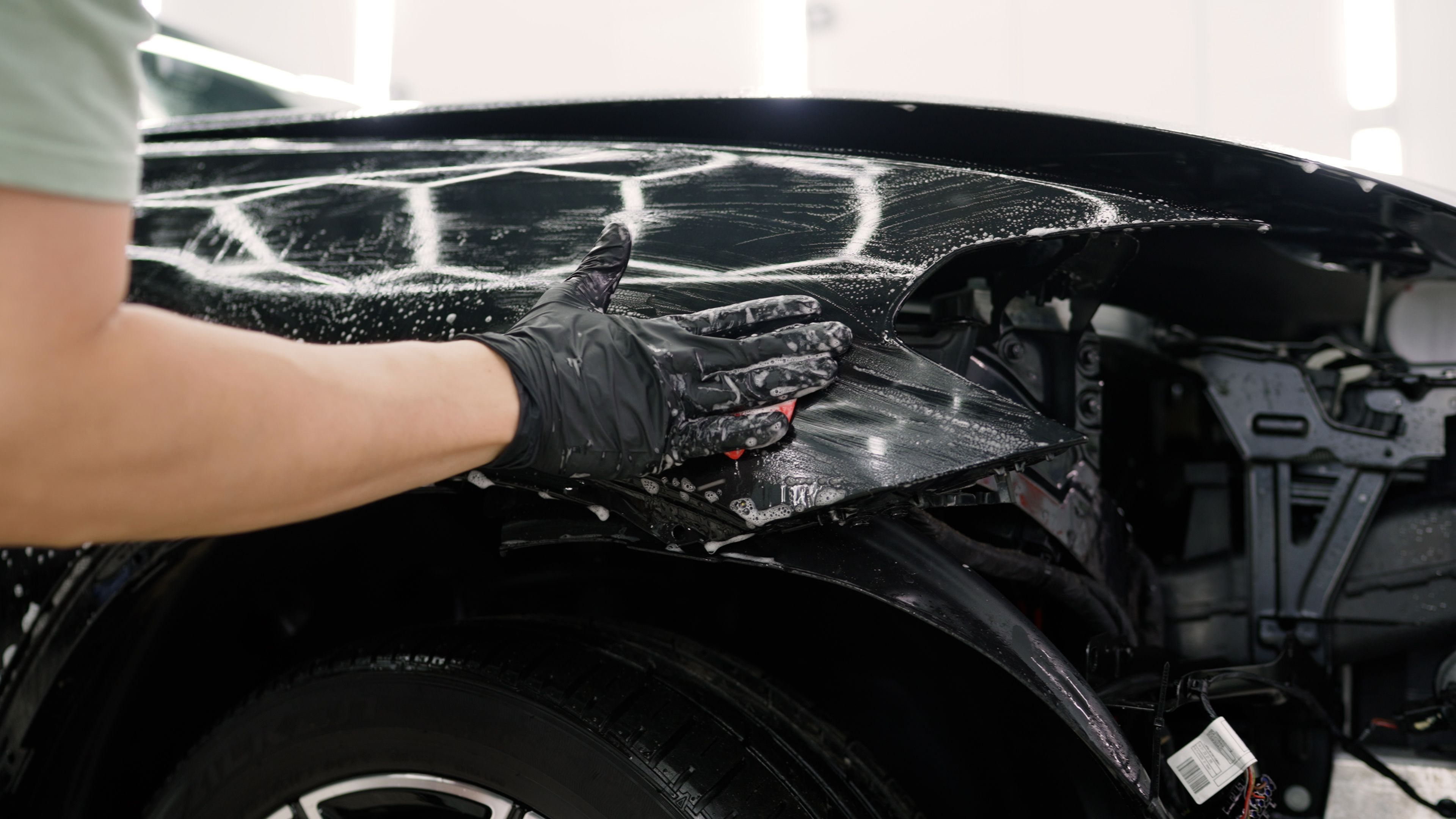Professional car detailer applying detergent with sponge on vehicle surface