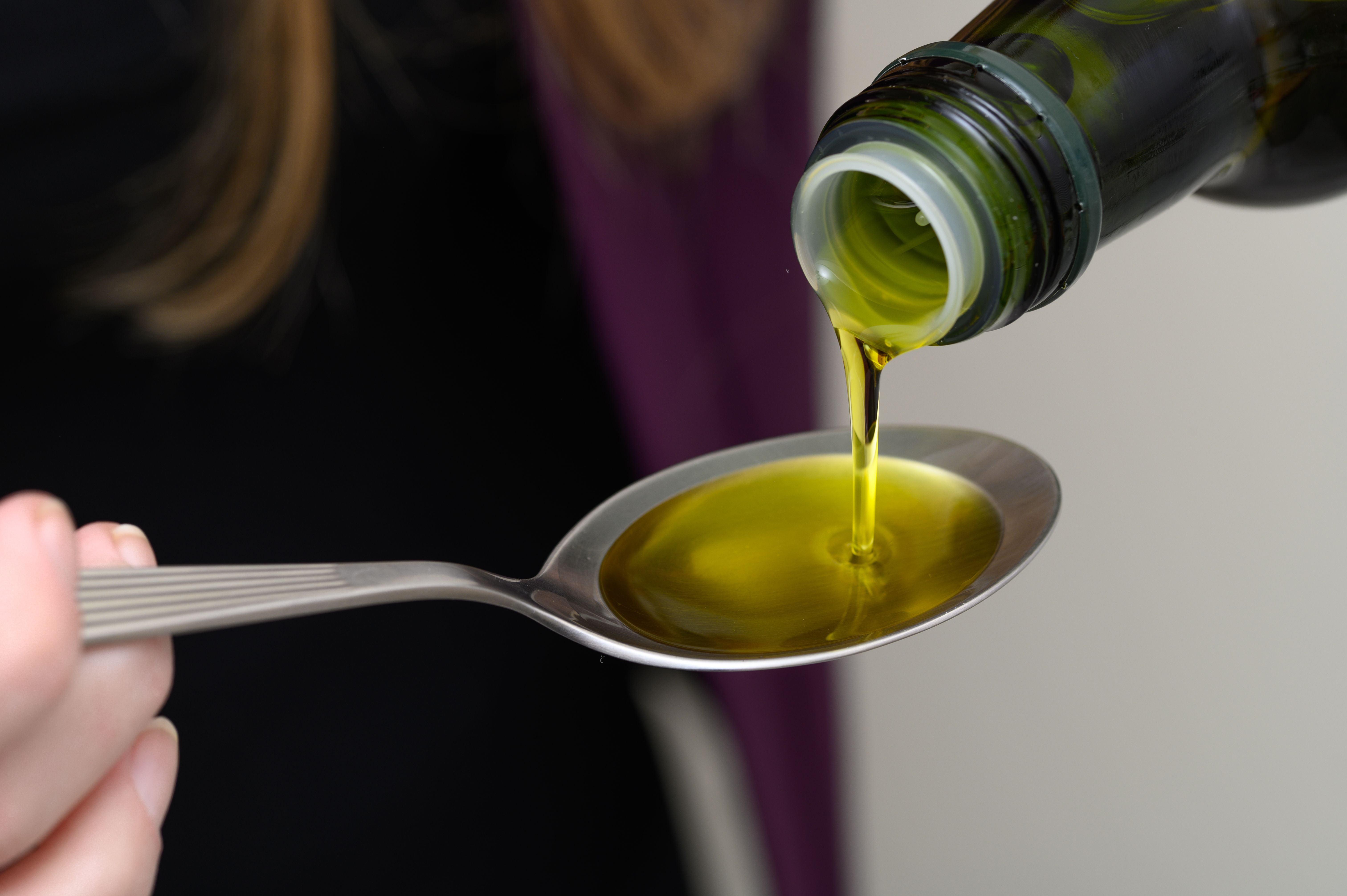 Woman pouring oil onto a spoon, healthy MCT oil Woman pouring oil onto a spoon, healthy MCT oil