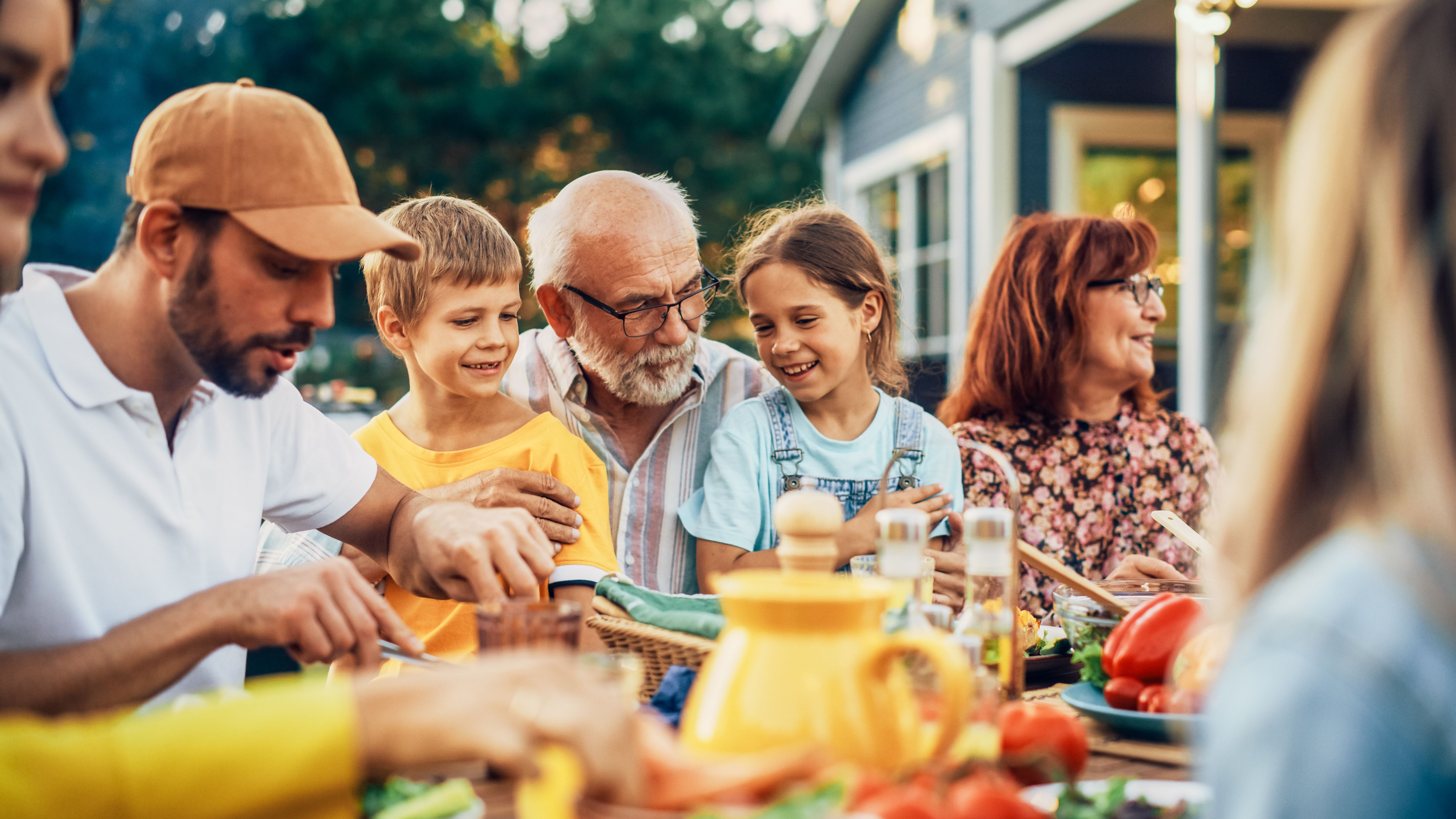 Portrait of a Happy Senior Grandfather Holding His Bright Talented Little Grandchildren on Lap at a Outdoors Dinner Party with Food and Drinks. Family Having a Picnic Together with Children. Portrait of a Happy Senior Grandfather Holding His Bright Talented Little Grandchildren on Lap at a Outdoors Dinner Party with Food and Drinks. Family Having a Picnic Together with Children.