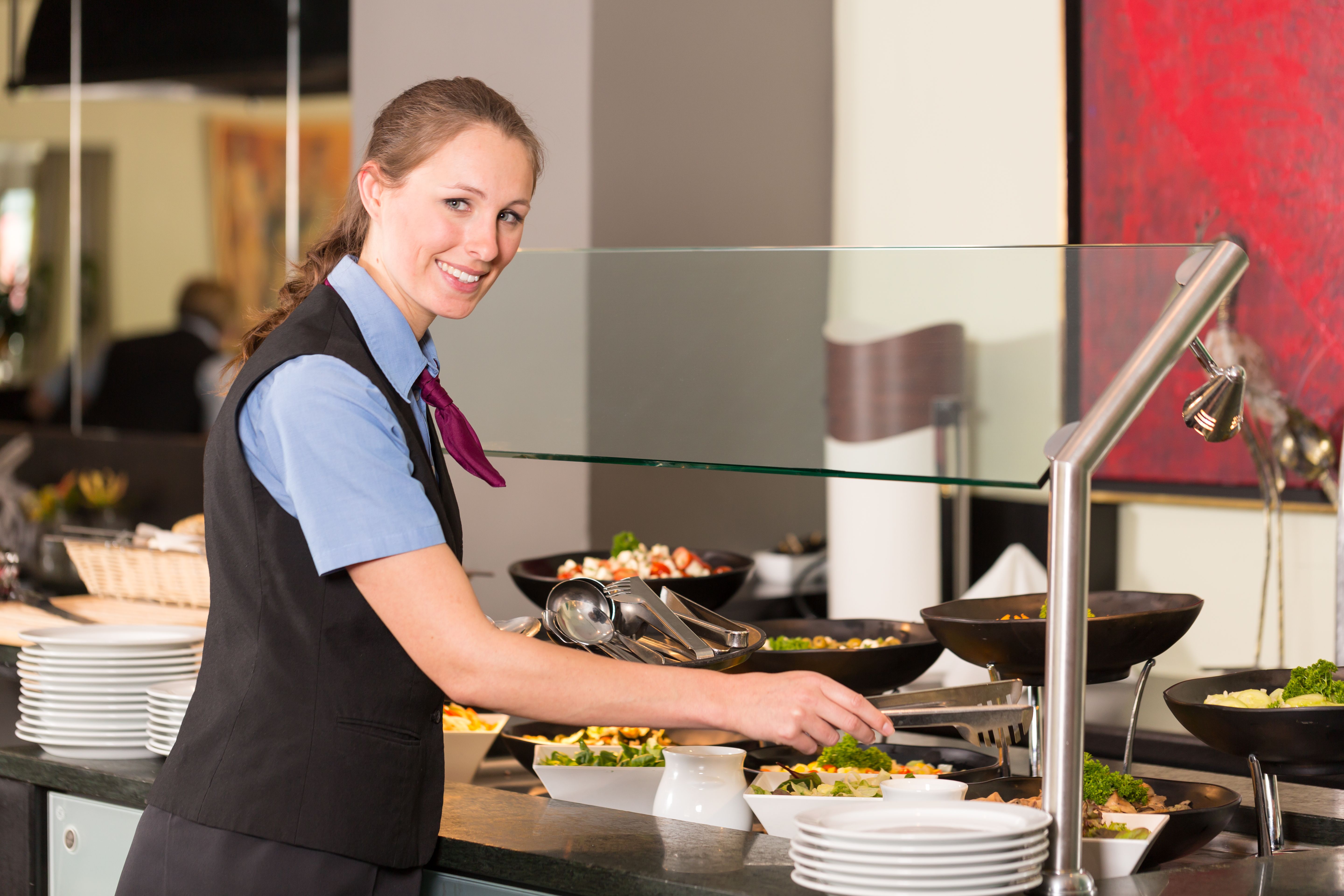 Waitress or catering professional putting food into buffet Waitress or catering professional putting food into buffet