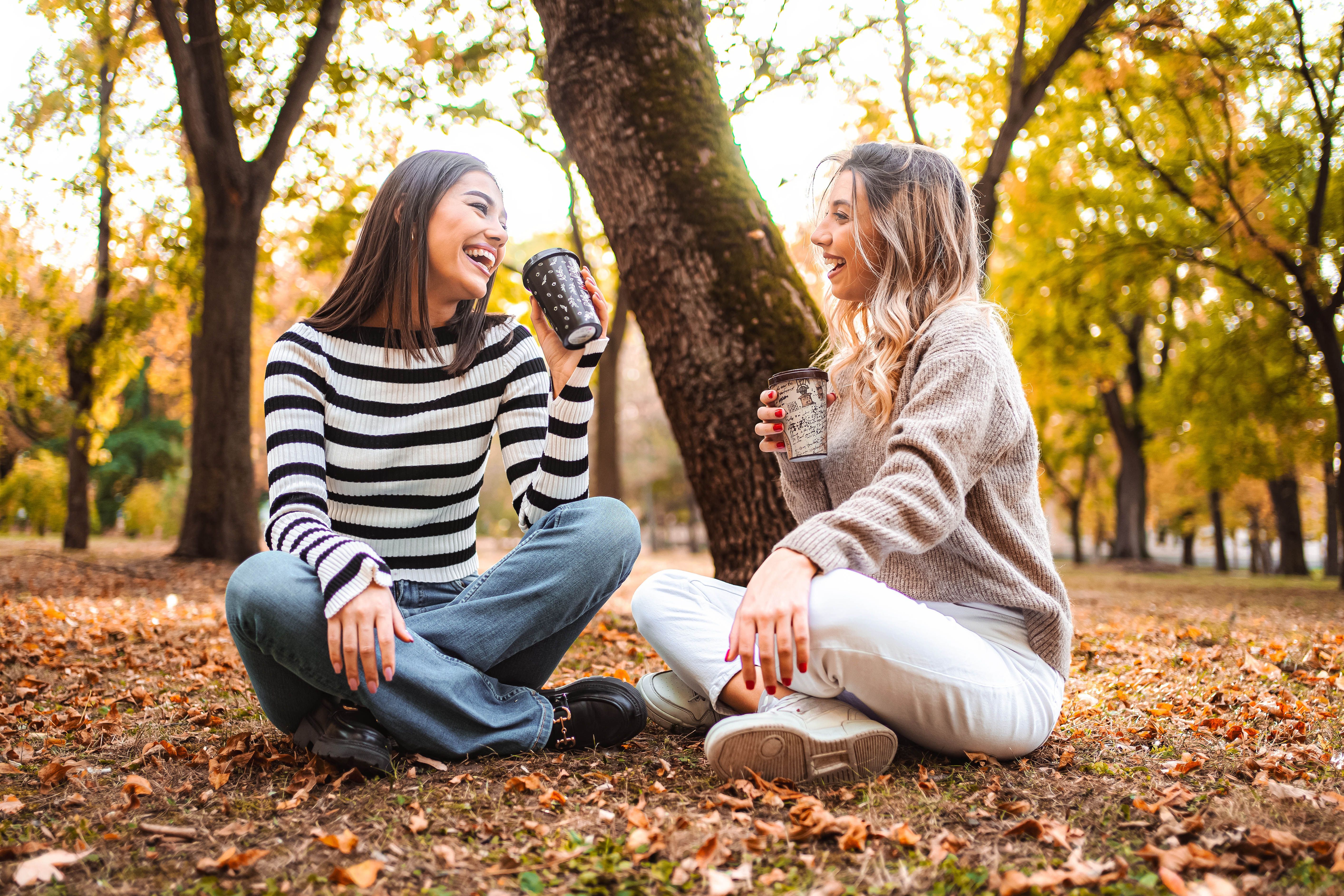 Two friends enjoying warm drinks in a colorful autumn park filled with leaves