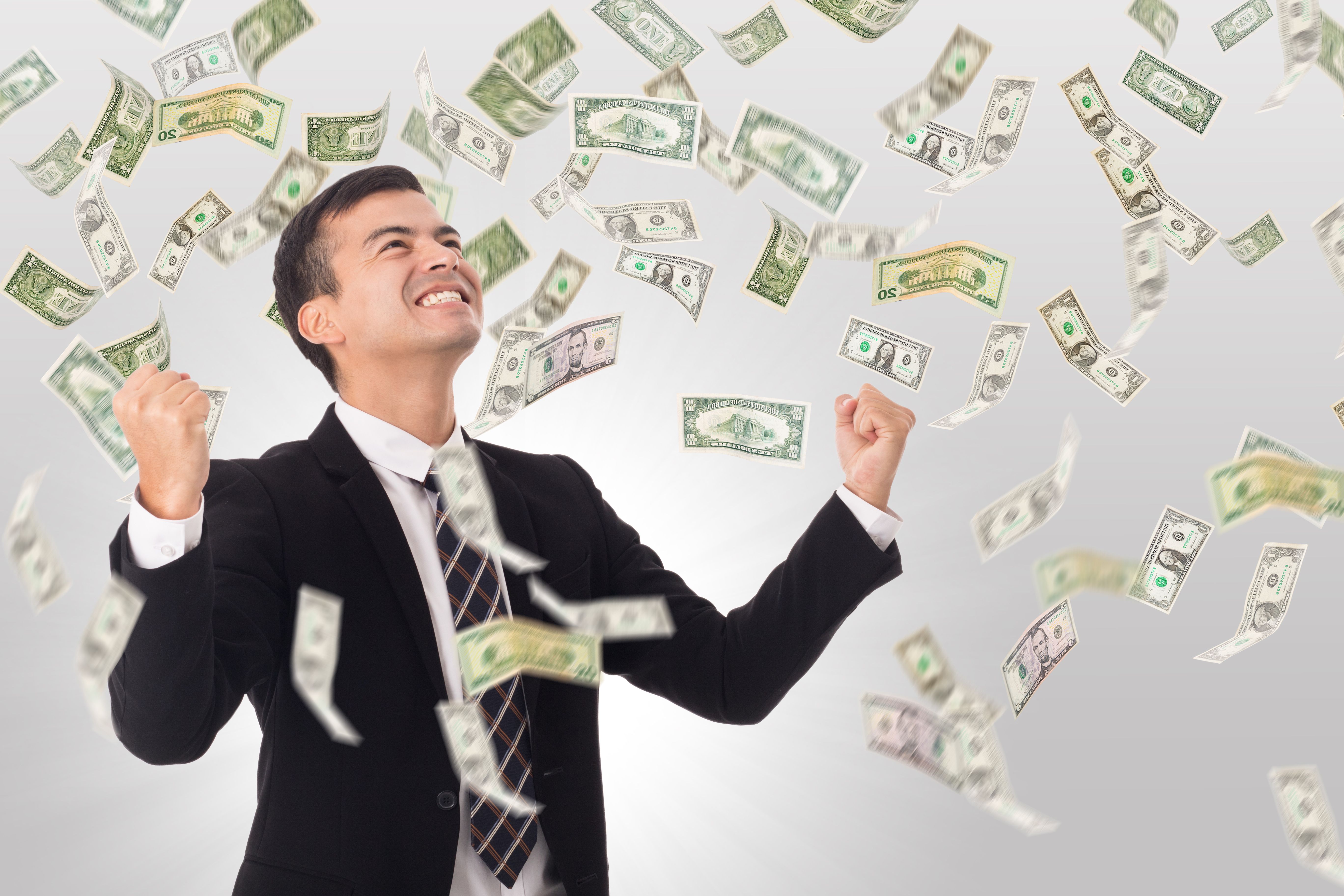 Business man looking up with triumphant smile and fists in the air as money rains down.
