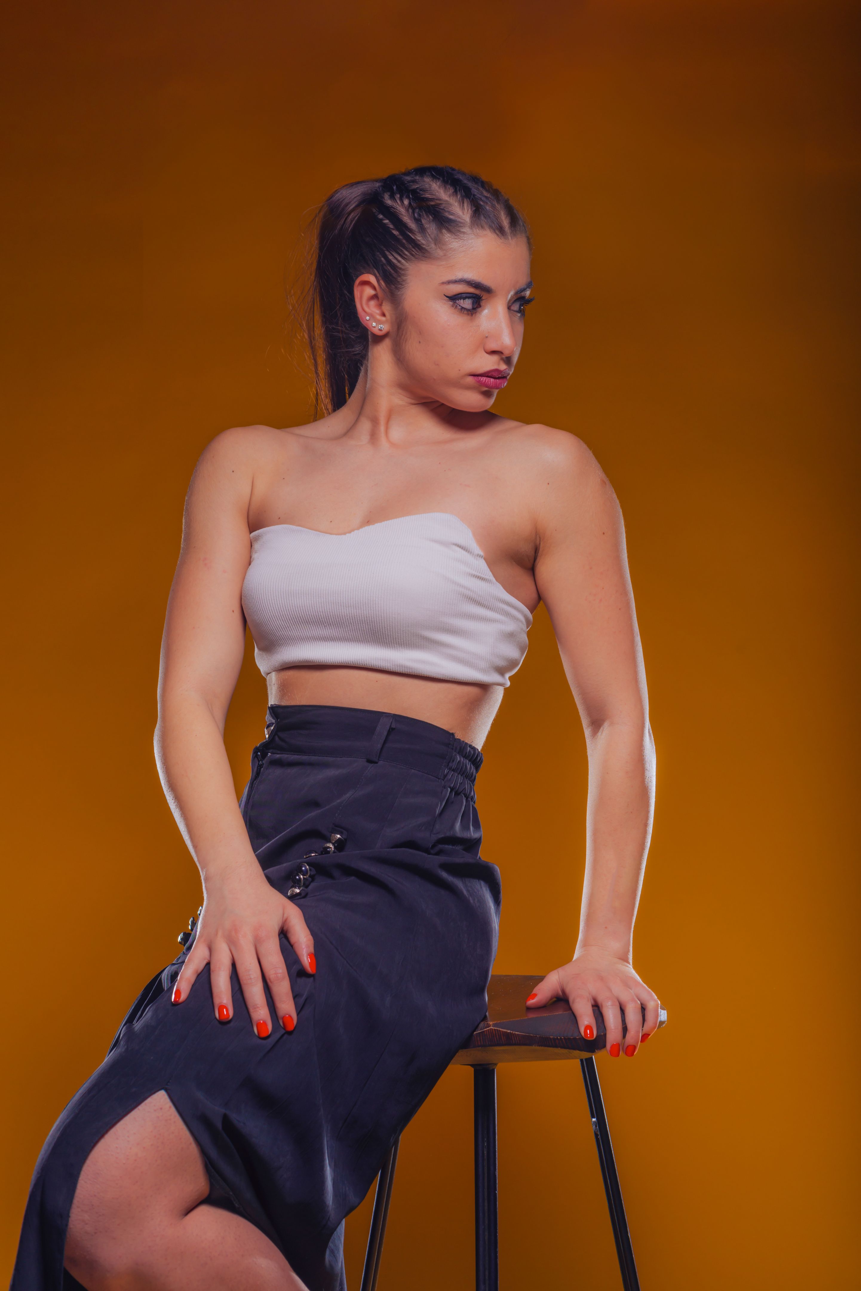 High fashion portrait of an attractive and stylish woman with dark hair and sexy neckline sitting on a high chair and posing inside a studio