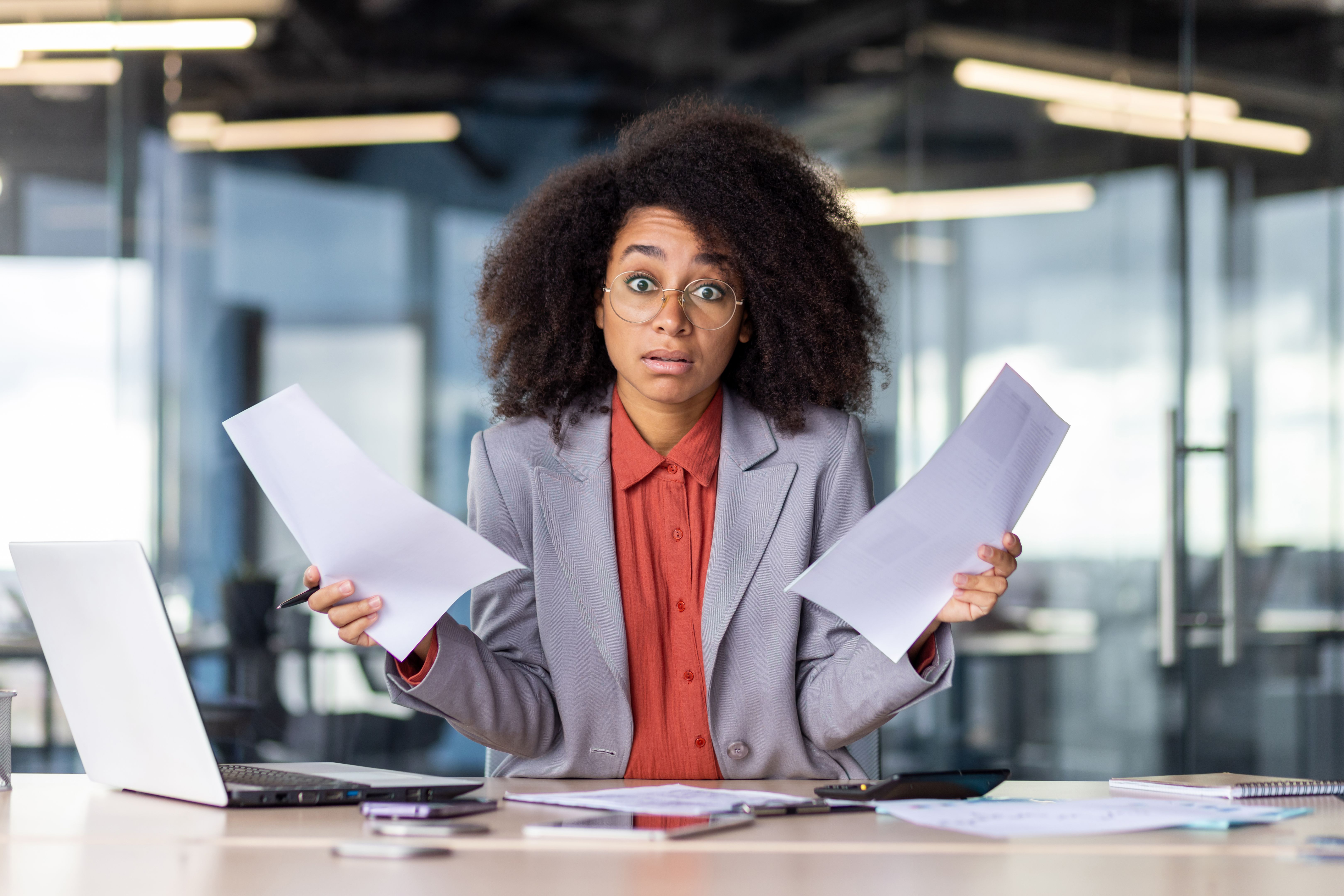 Surprised businesswoman in office holding papers, overwhelmed with workload