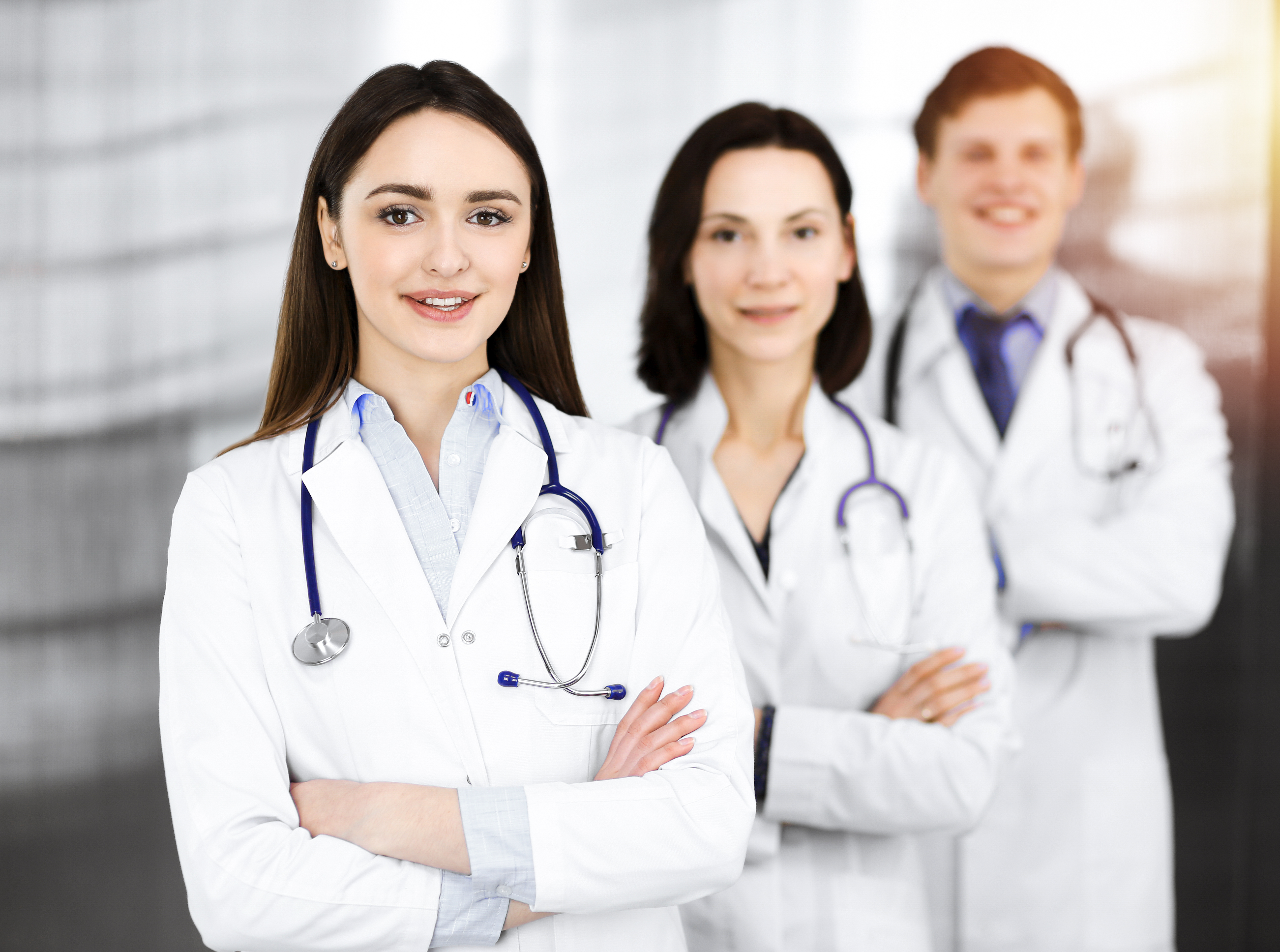 Group of young professional doctors standing as a team with arms crossed in sunny hospital. Medical help, insurance in health care, best disease treatment and medicine concept