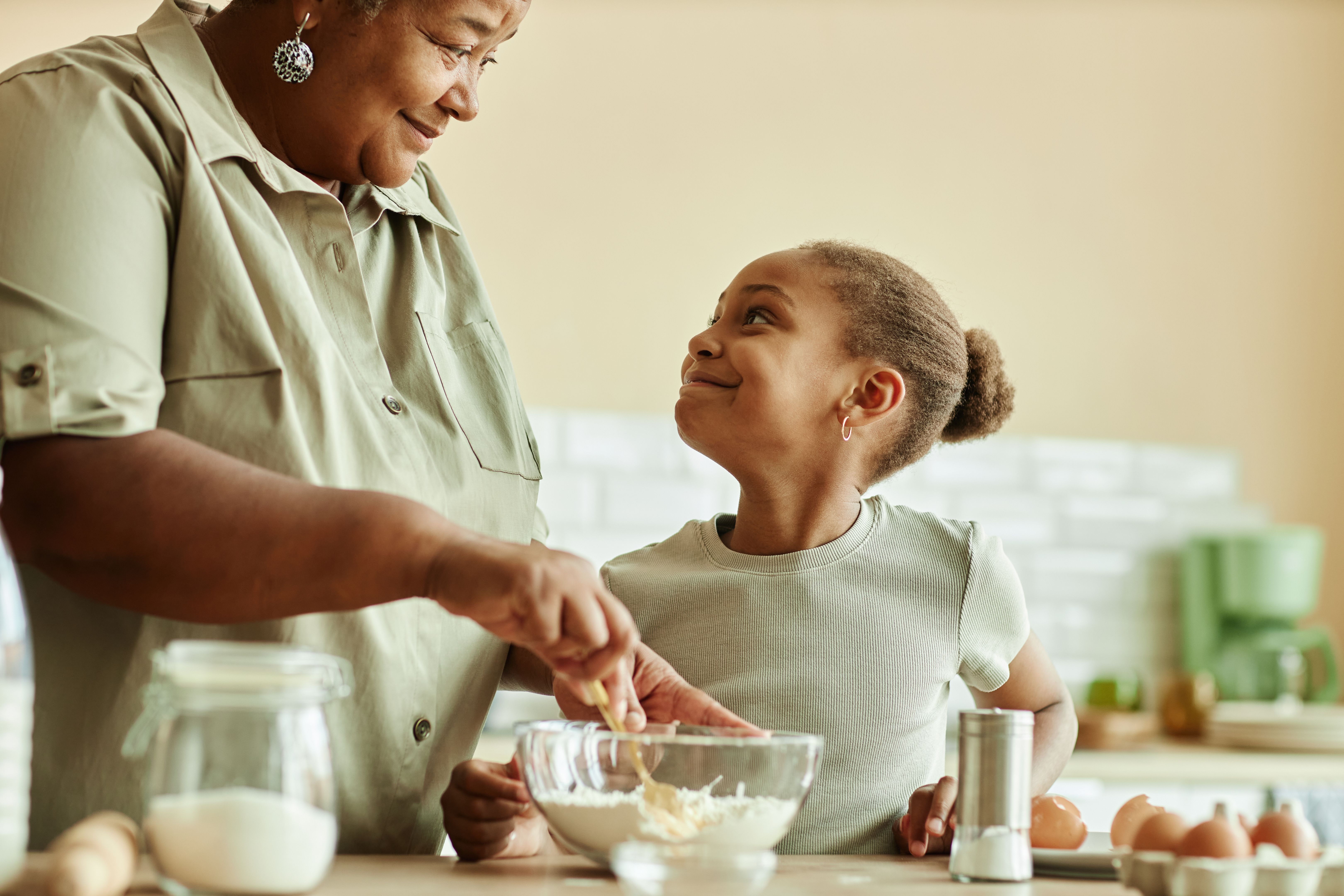 Smiling Black Child Looking at Grandma Cooking Together at Kitchen