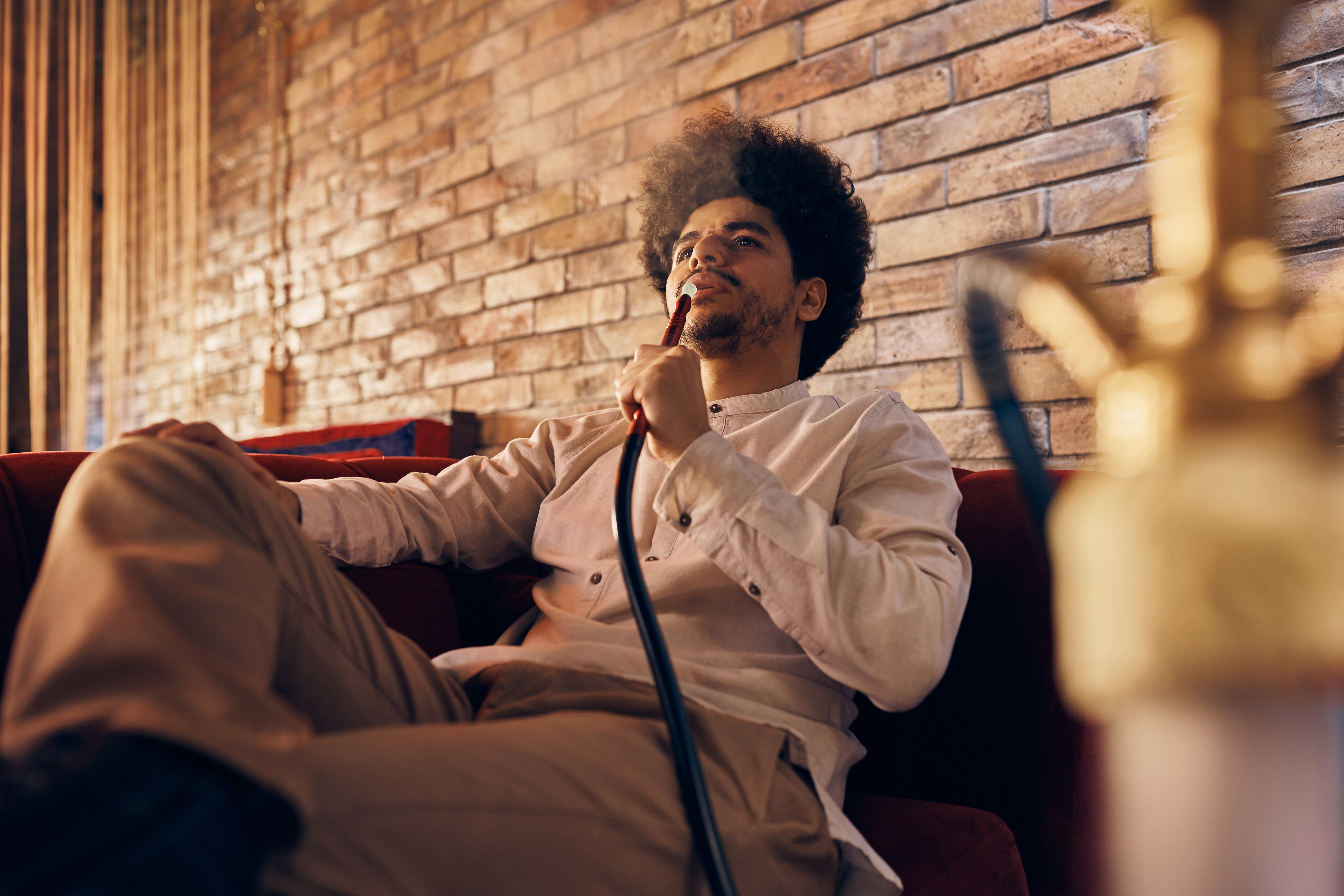 Young Arabian man relaxing while smoking shisha at home. Young Arabian man relaxing while smoking shisha at home.