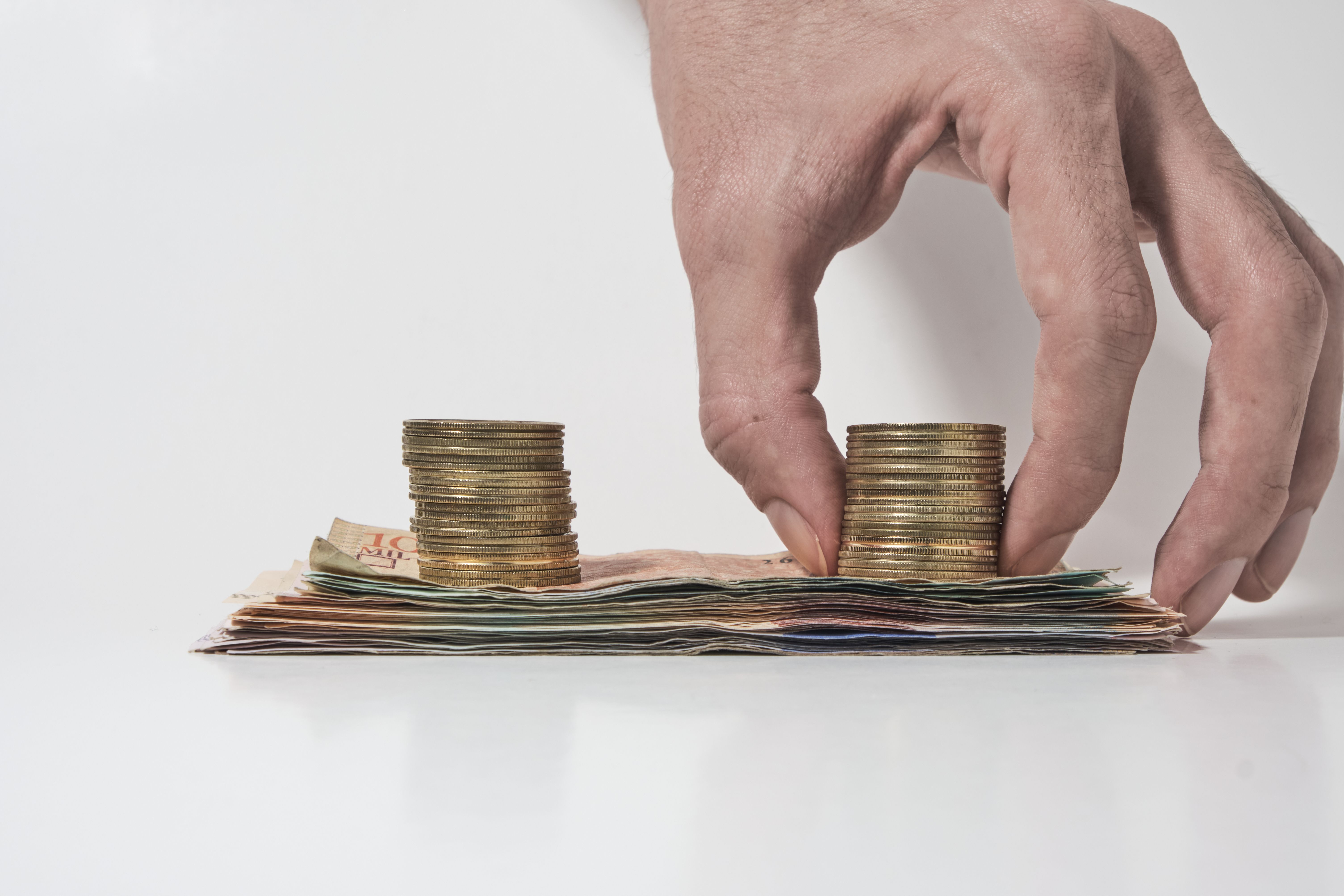mano recogiendo monedas sobre una pila de billetes sobre un fondo blanco